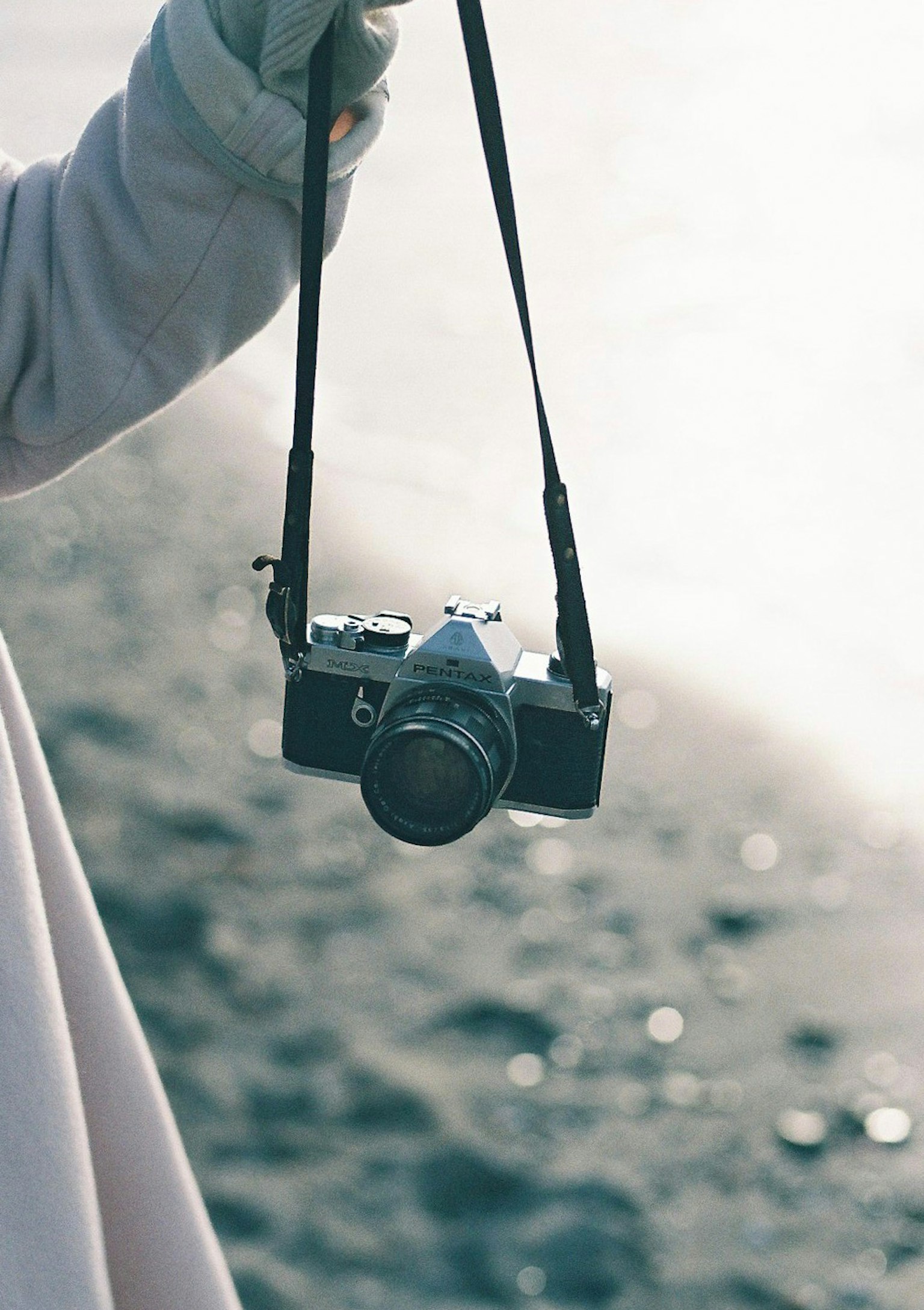 Una mano che tiene una macchina fotografica appesa a una tracolla sulla spiaggia