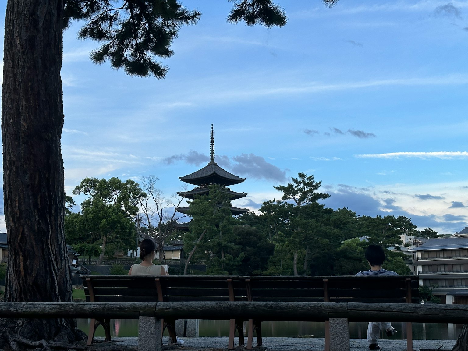 两个人坐在长椅上，背景中有一座塔