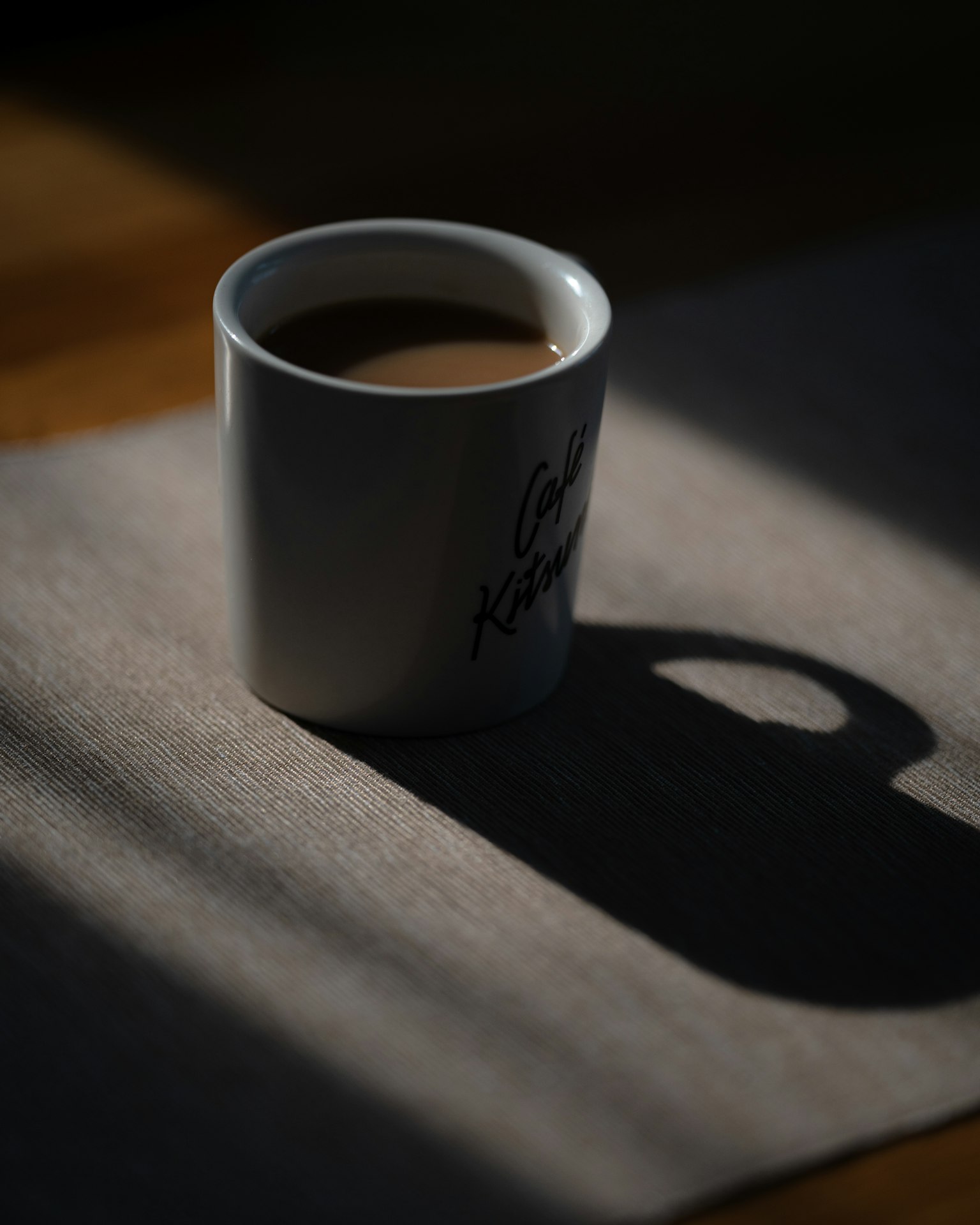 Una tazza bianca piena di caffè posata su un tavolo che proietta un'ombra