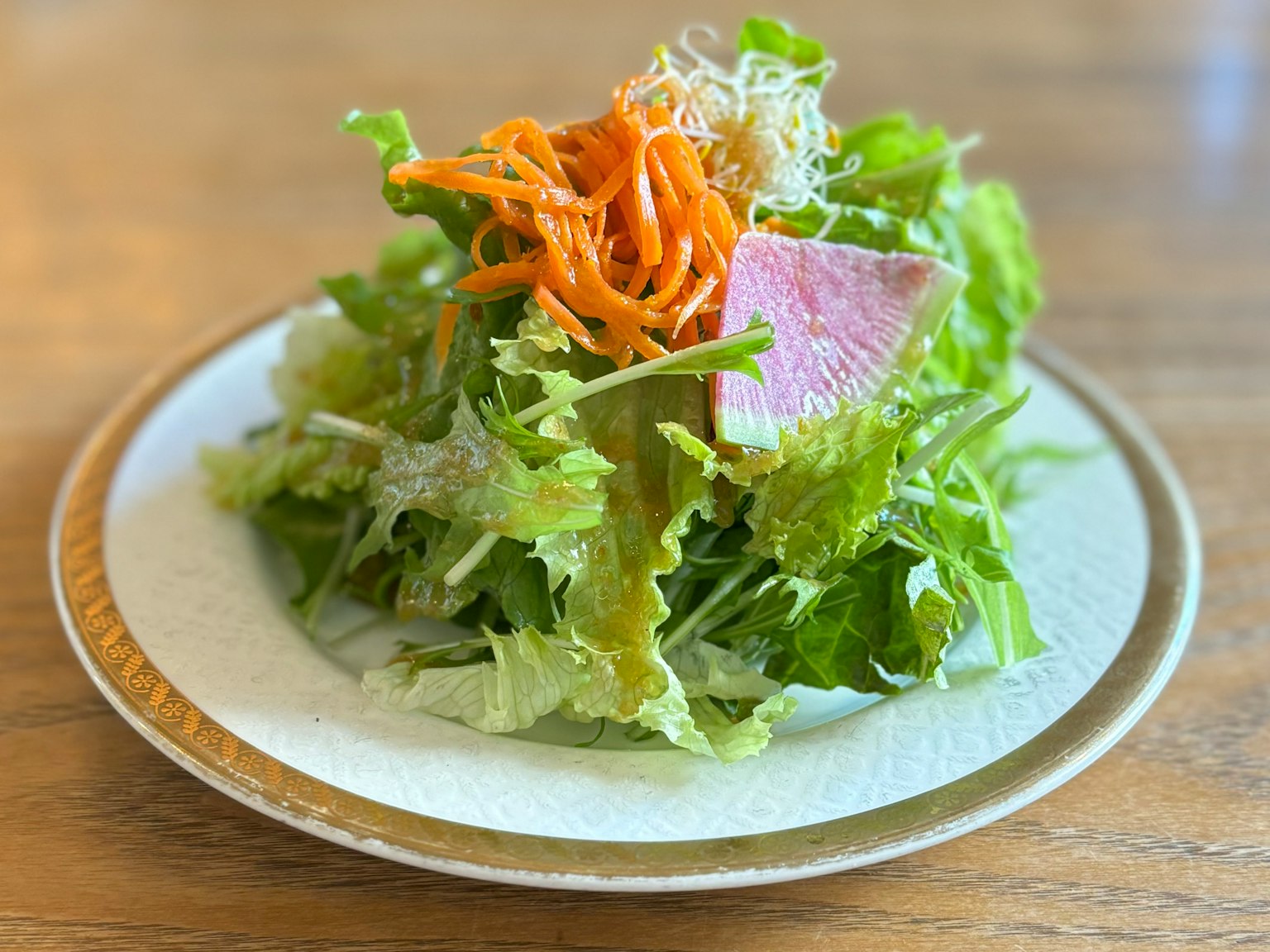 Ein Teller mit frischem Salat aus Kopfsalat und Karotten, garniert mit Schinkenscheiben
