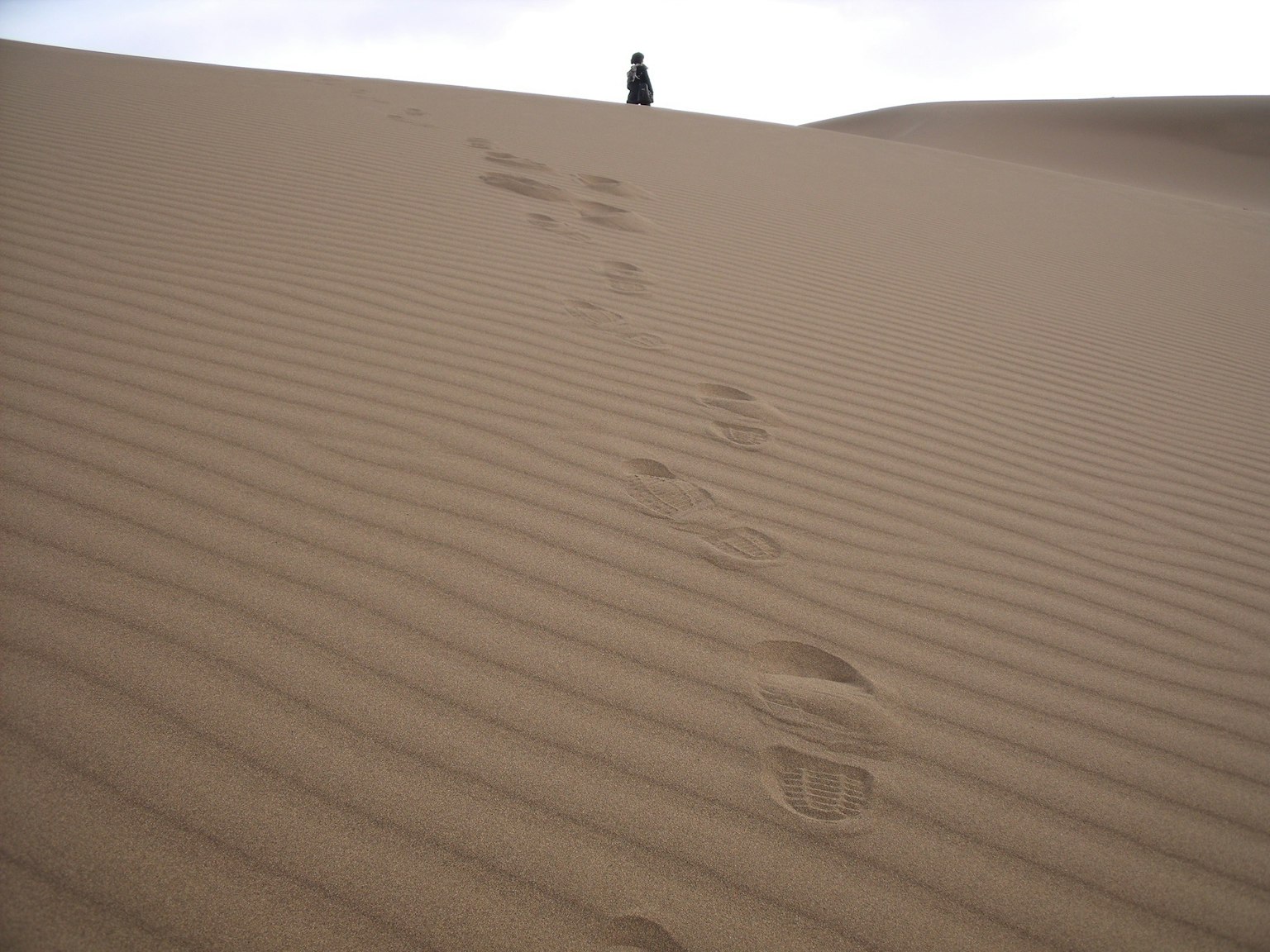Footprints on a sand dune with a figure in the distance