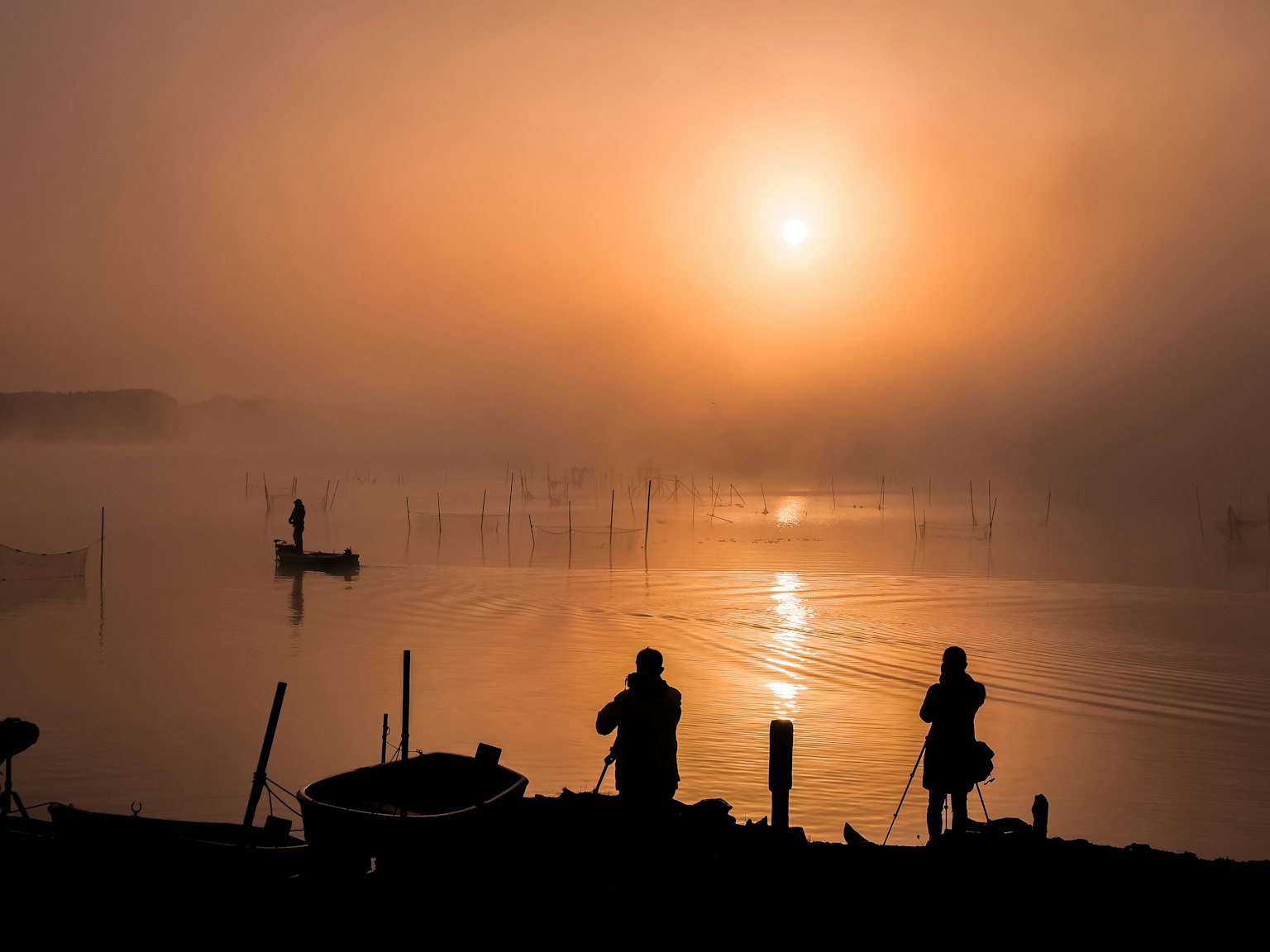 Silhouette di due pescatori nella nebbia con alba arancione