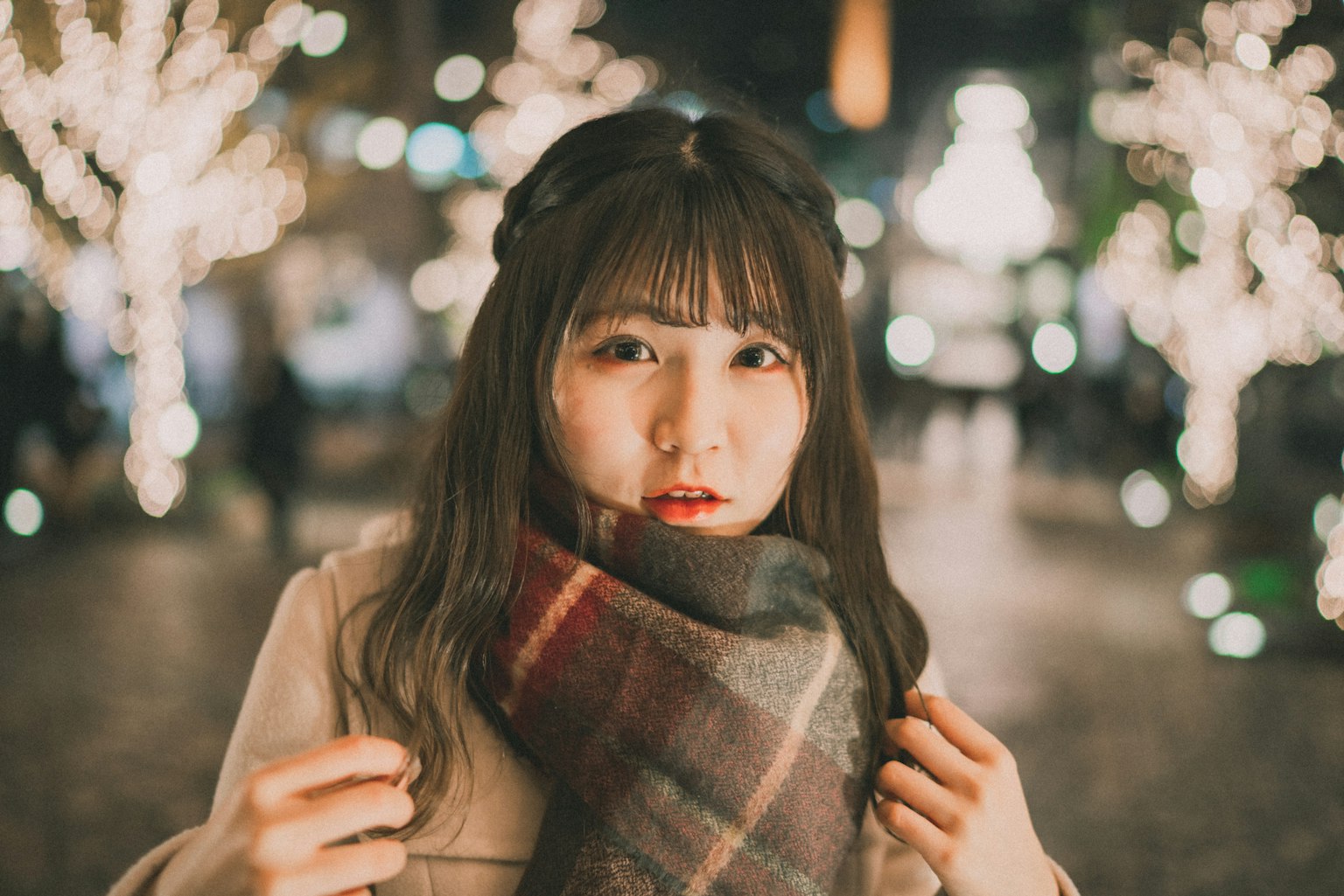 Một người phụ nữ trong khăn quàng nhìn về phía máy ảnh trên đường phố sáng đèn vào ban đêm