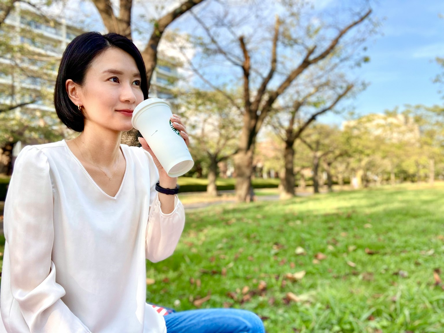 女性在公园中享用咖啡，背景是树木