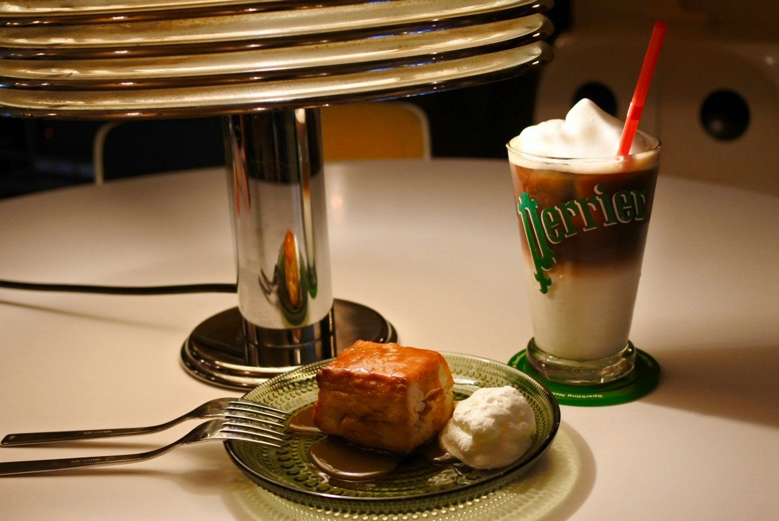 Scène de dessert et de boisson sur une table avec un café glacé surmonté de crème à côté d'une part de gâteau servie avec de la crème fouettée et une fourchette