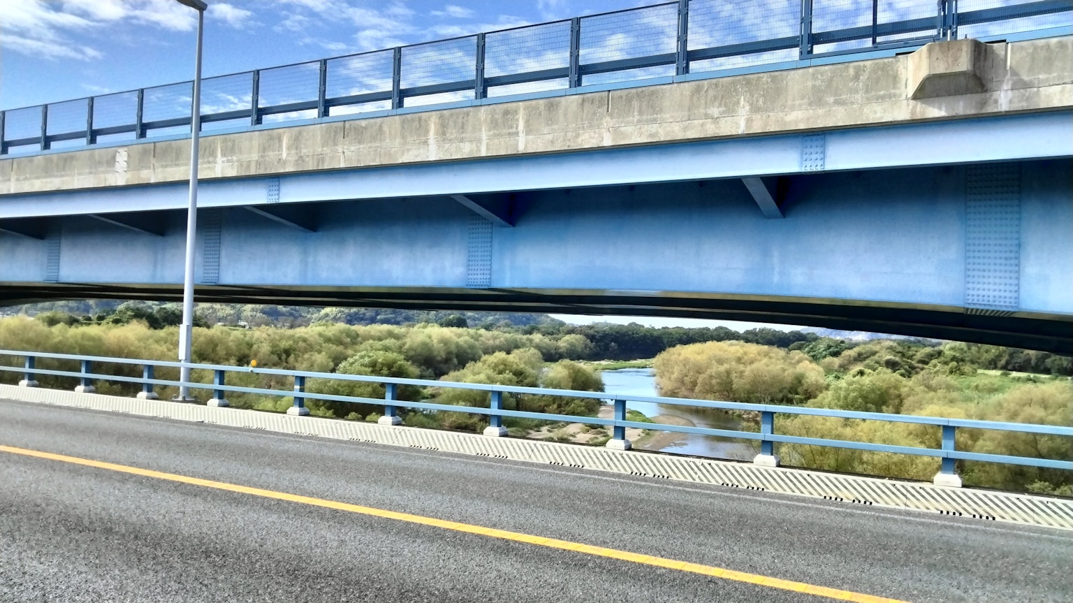 Un pont bleu au-dessus d'une rivière avec une végétation luxuriante en dessous