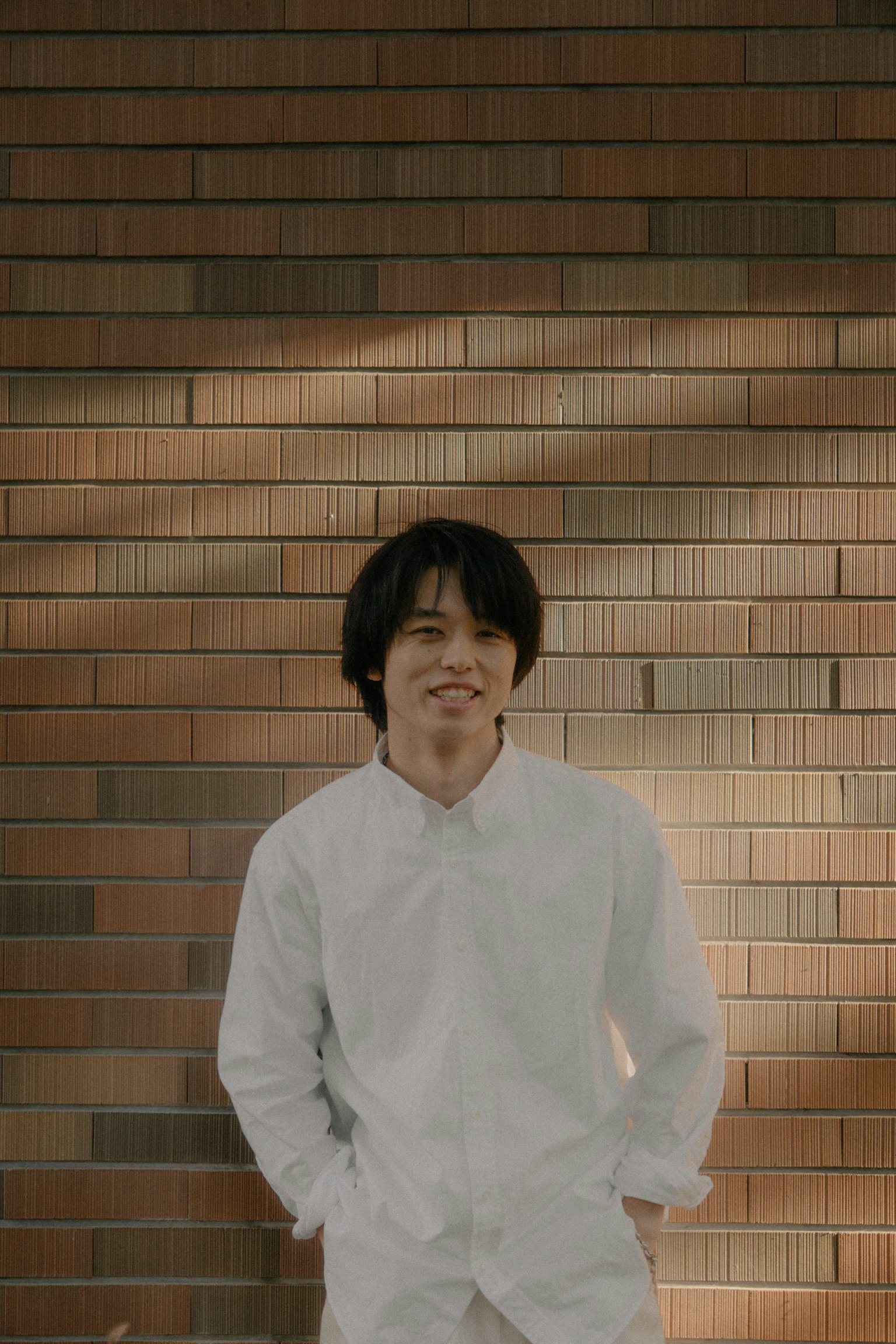 一個穿著白襯衫的男人在磚牆前微笑