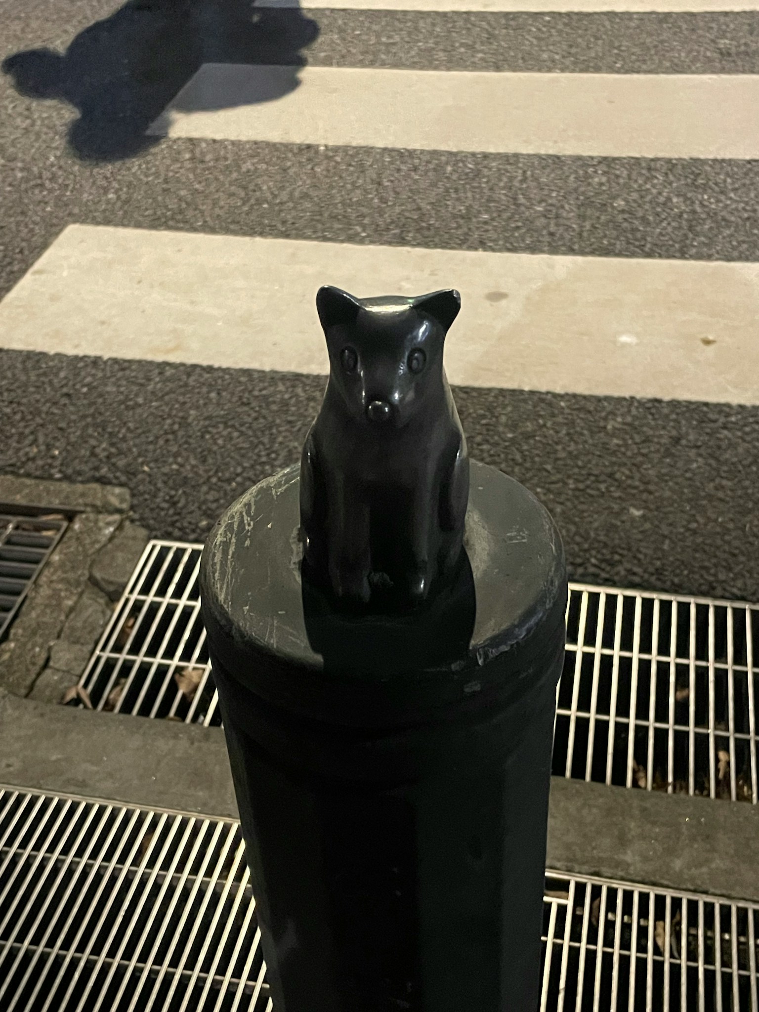 黒い猫の彫刻が横断歩道のポールの上に置かれている