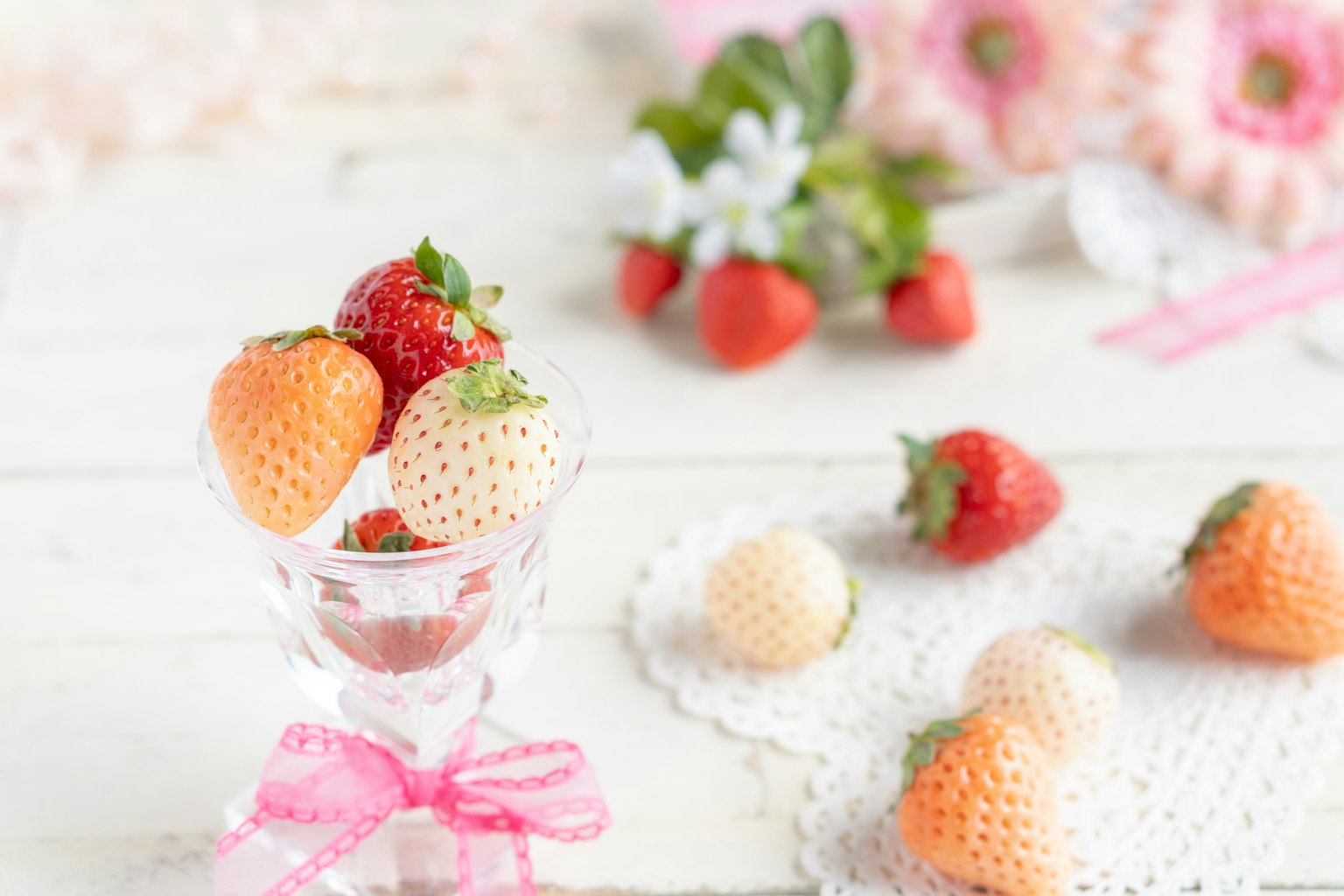 Fragole di diversi colori in una tazza trasparente con fiori sullo sfondo