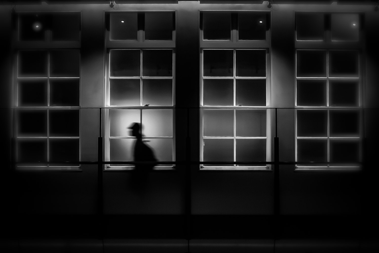 Silueta de una persona caminando frente a ventanas débilmente iluminadas