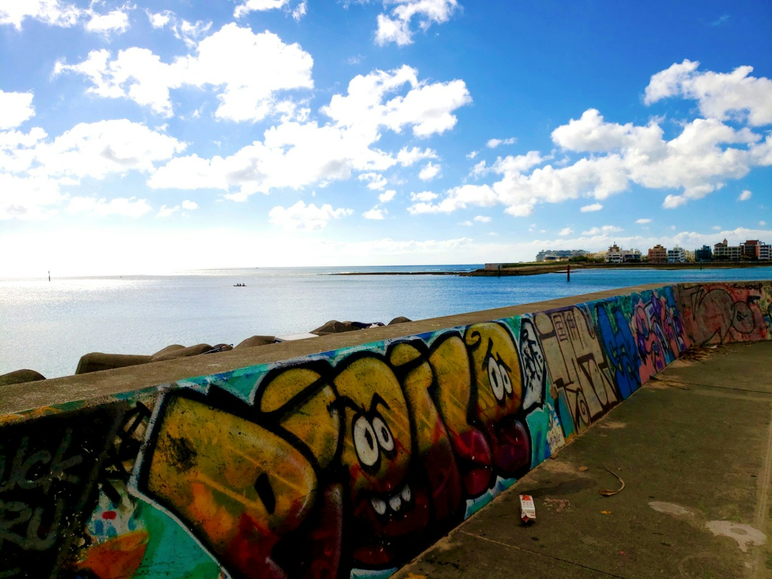 Bức tường graffiti đầy màu sắc với những chữ cái sống động dưới bầu trời xanh và mây nhìn ra biển yên tĩnh