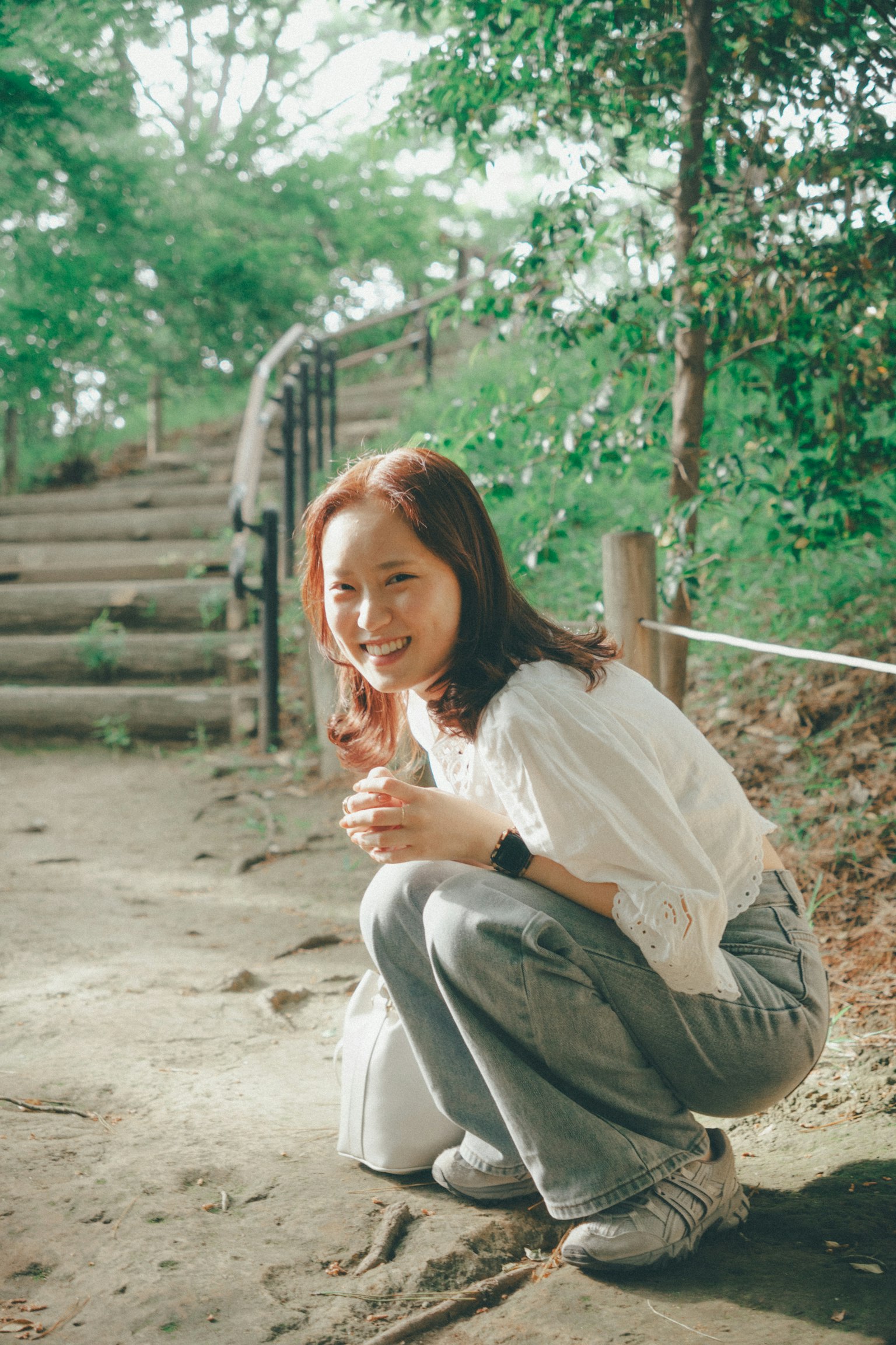 초록색 배경에서 쪼그리고 앉아 미소 짓고 있는 여성 흰색 상의와 청바지 착용