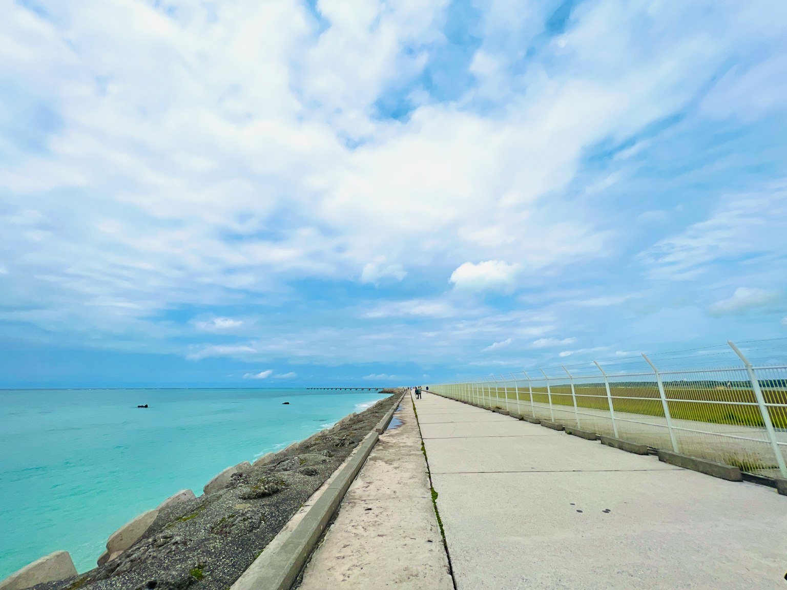 Betonweg, der zu einem blauen Meer unter einem bewölkten Himmel führt