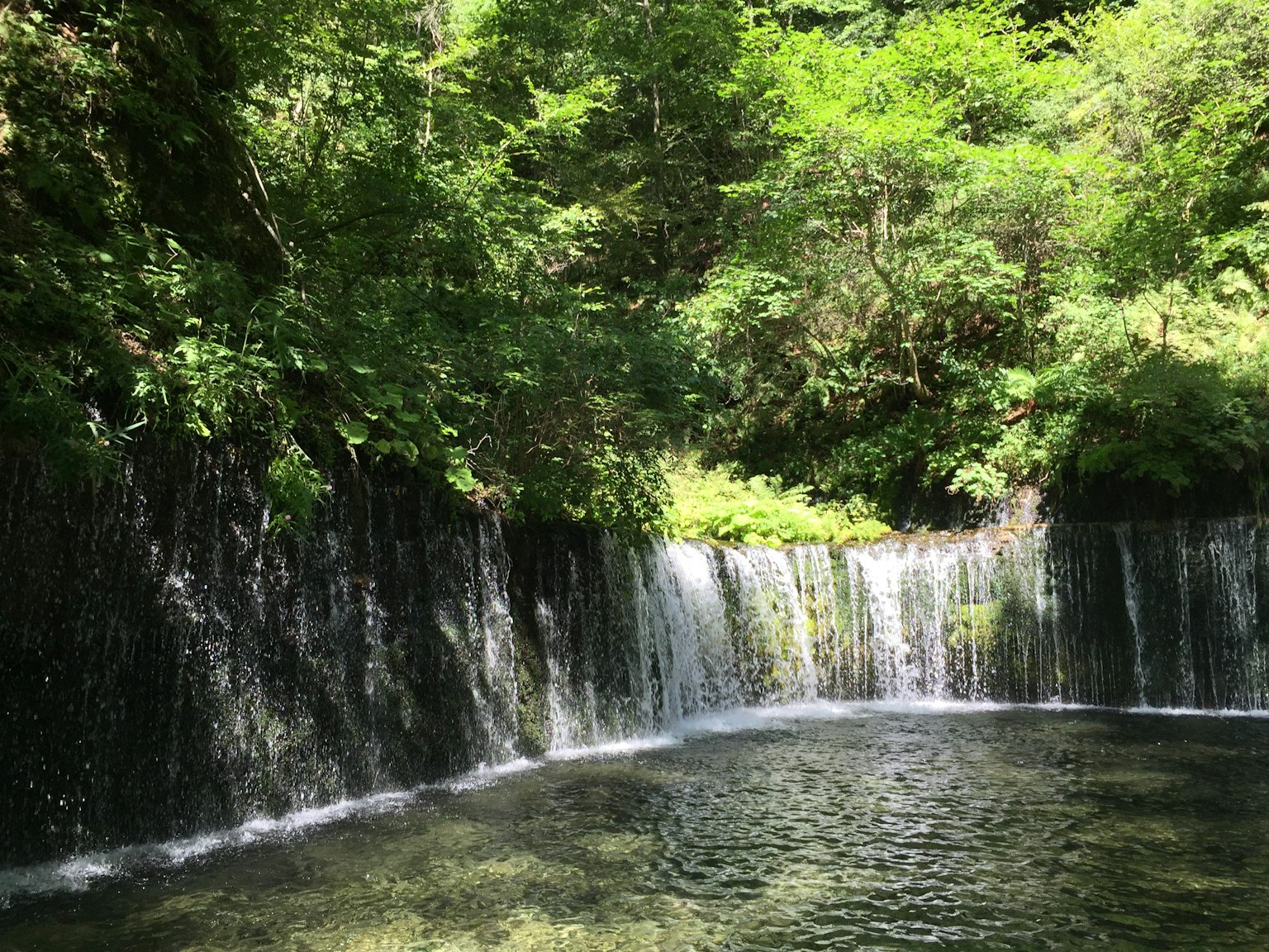 Air terjun dikelilingi oleh pepohonan rimbun dan permukaan air tenang