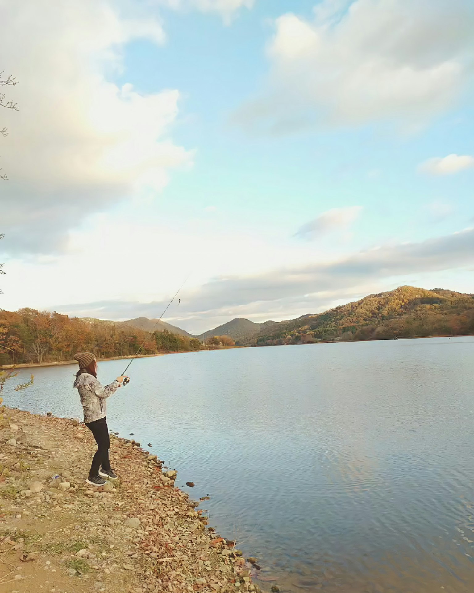 Person, die am See mit Bergen im Hintergrund angelt