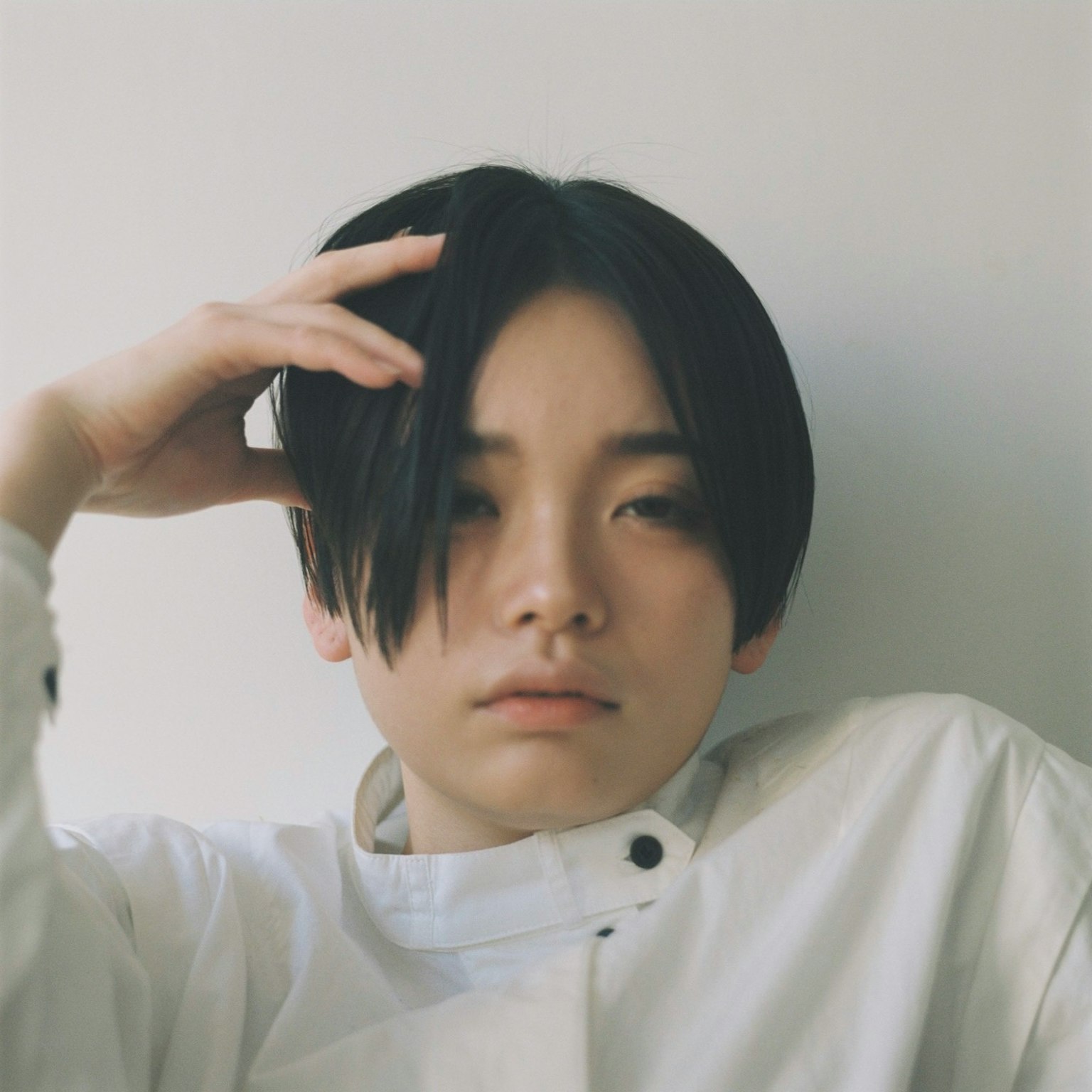 A young person in a white outfit appears thoughtful with a hand on their head