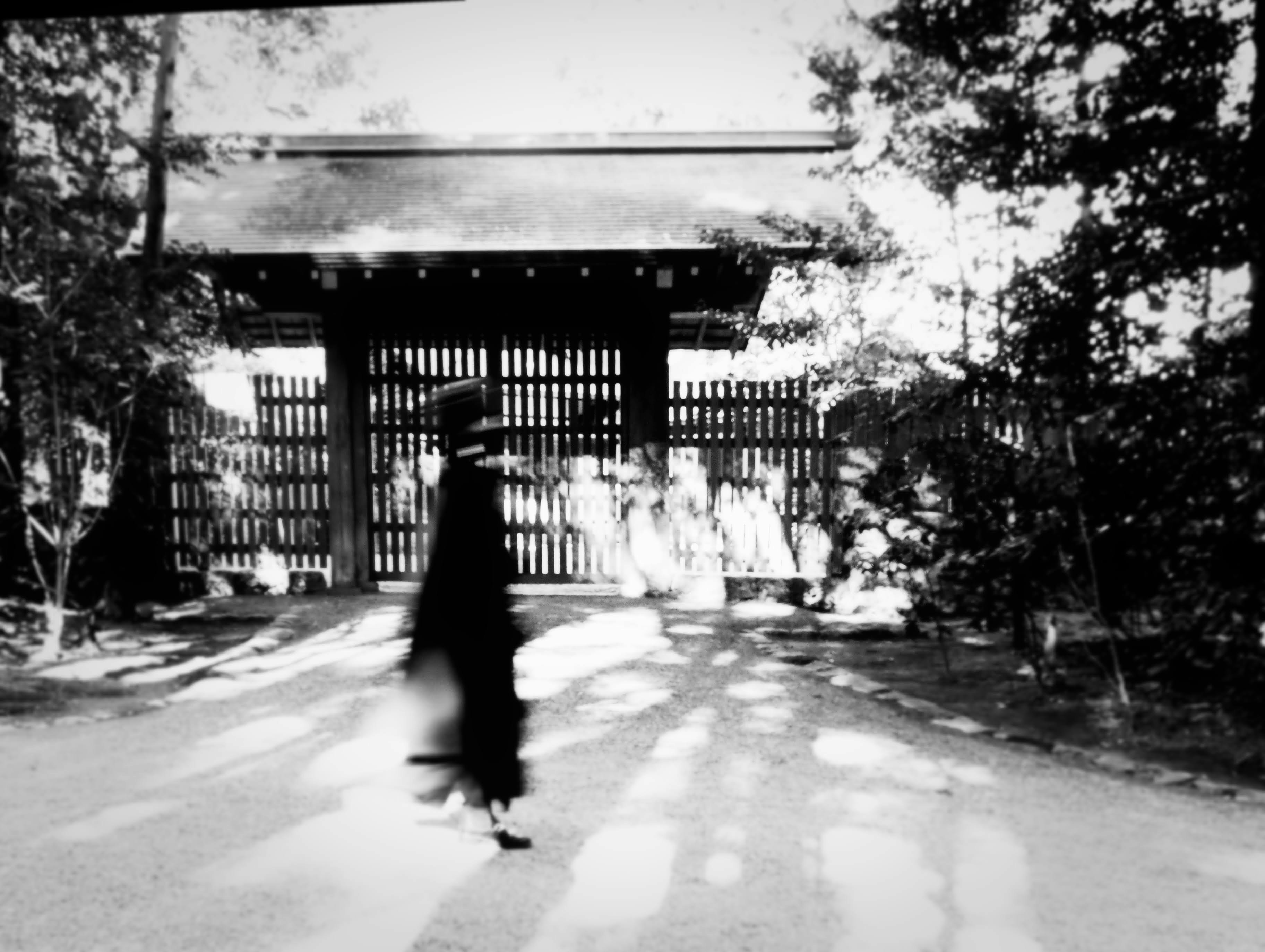 モノクロの路地を歩く人物と門構えの建物