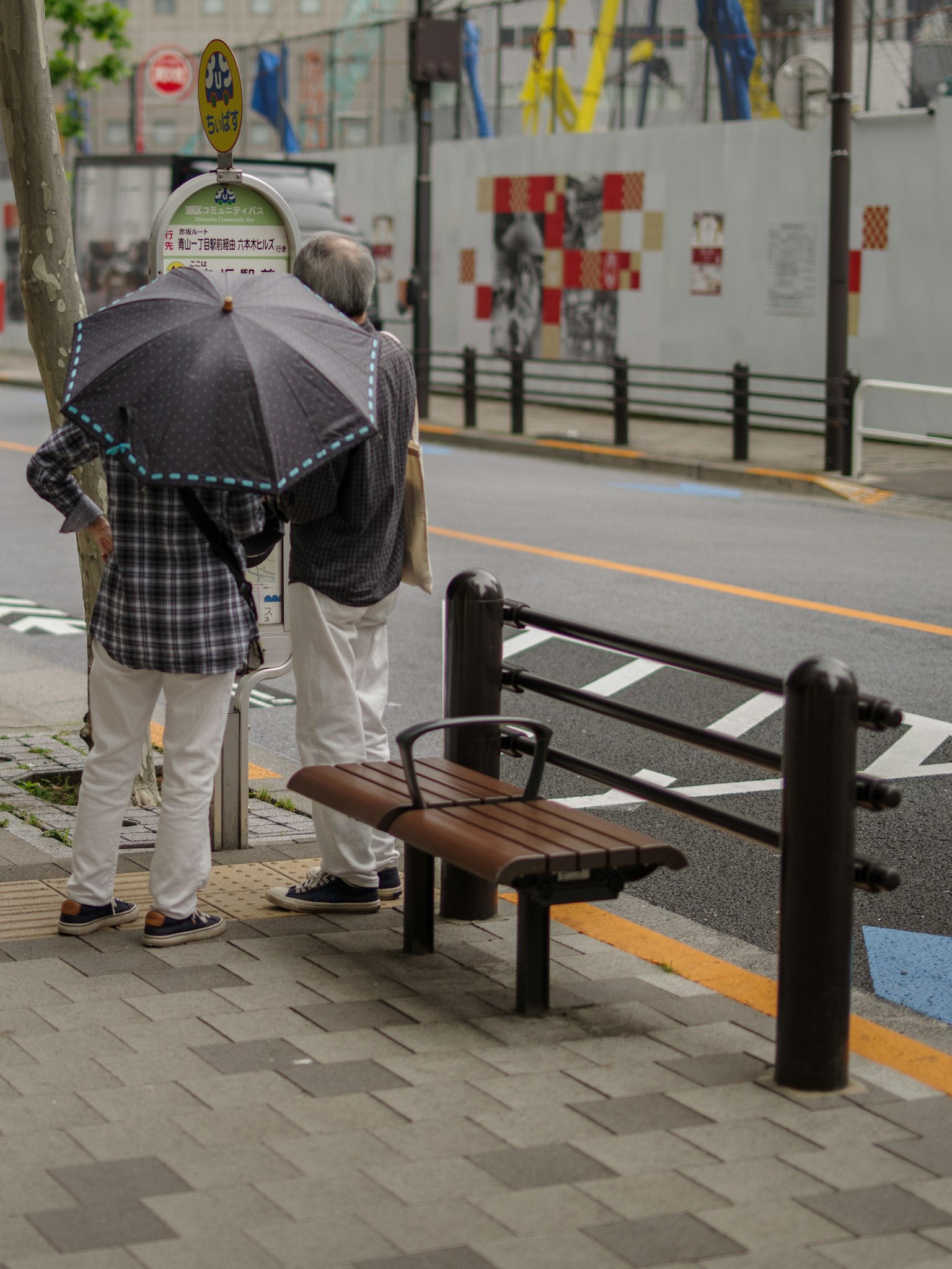 两个人拿着伞站在城市街道的长椅旁边