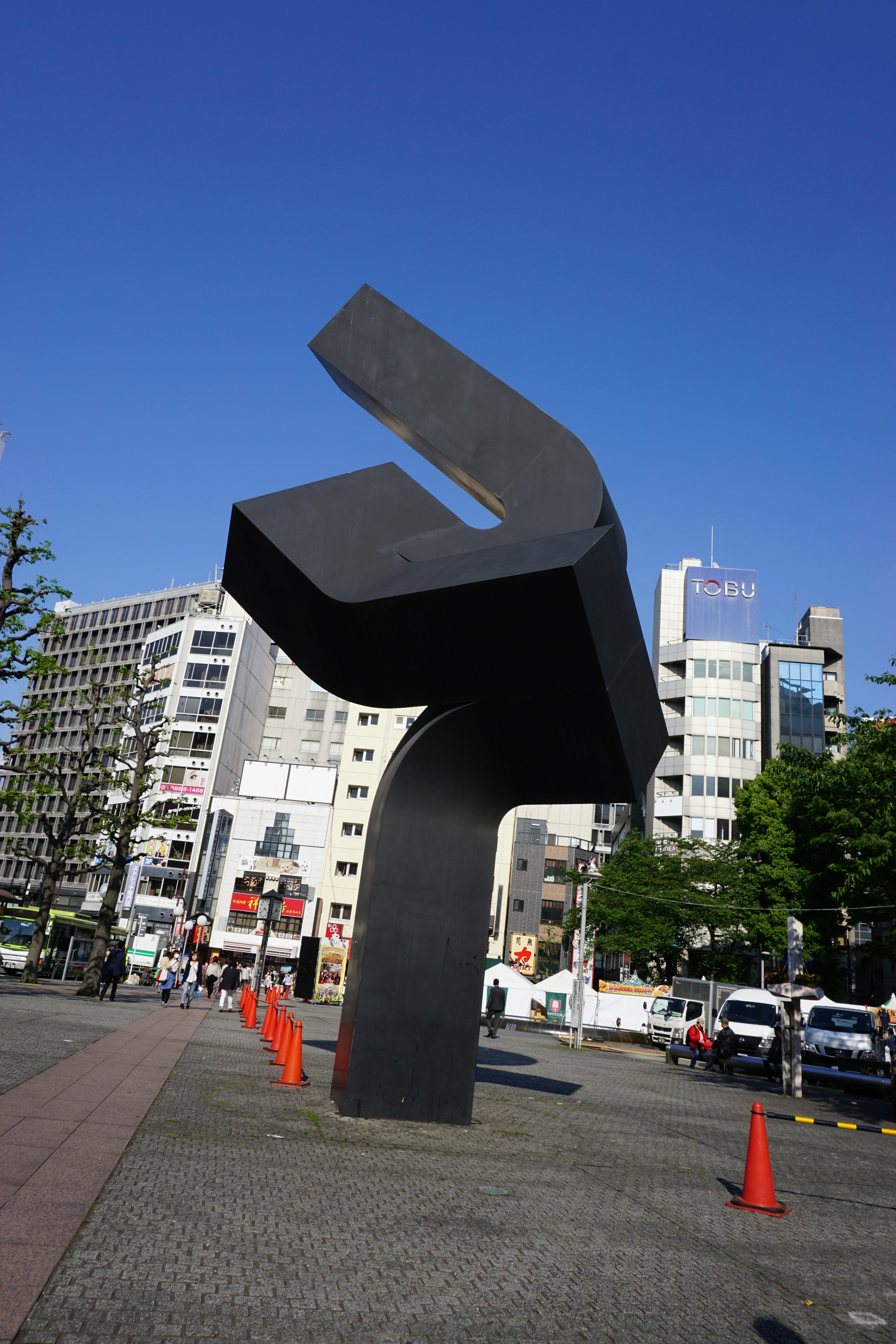 riesiges schwarzes Denkmal auf einem städtischen Platz unter klarem blauem Himmel