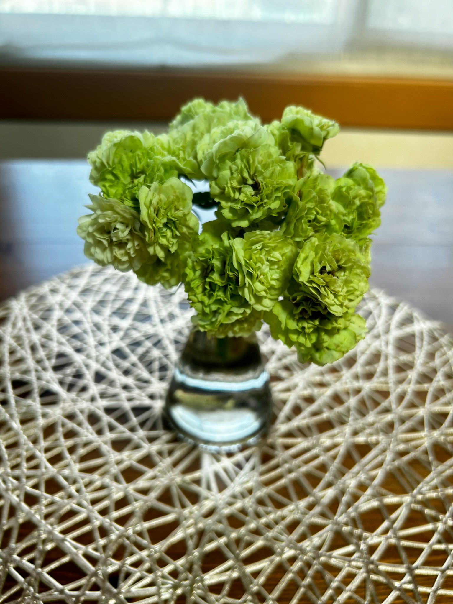 Un vaso trasparente con fiori verdi su un centro tavola intrecciato