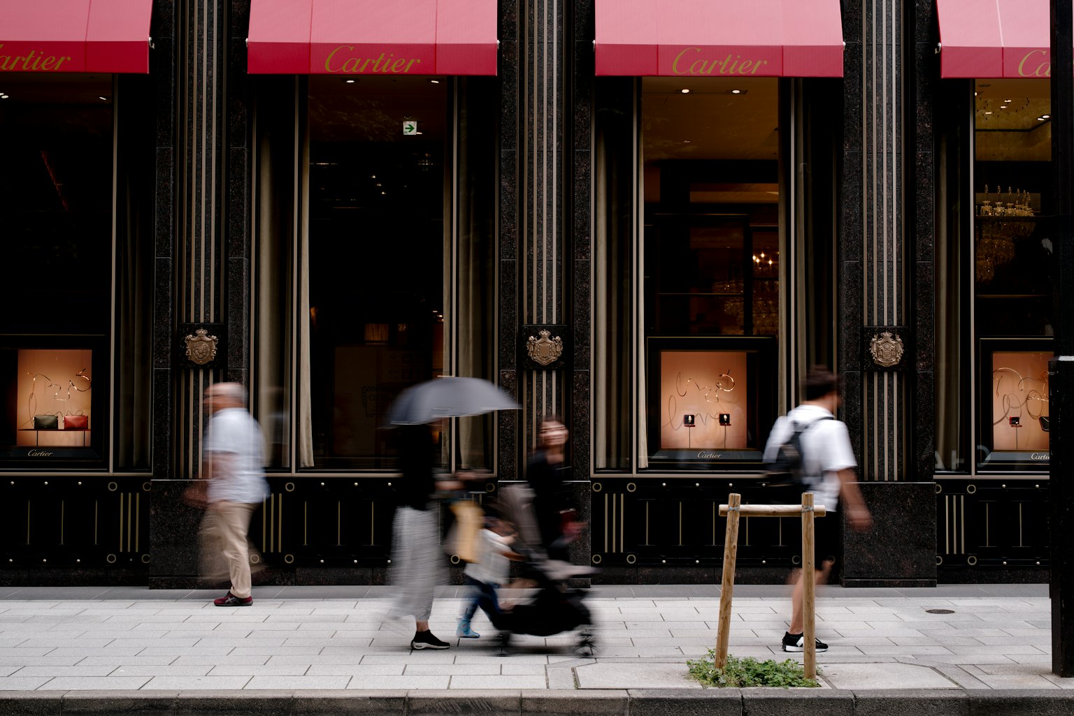 Des gens marchant avec des parapluies dans une scène urbaine avec un bâtiment aux auvents rouges