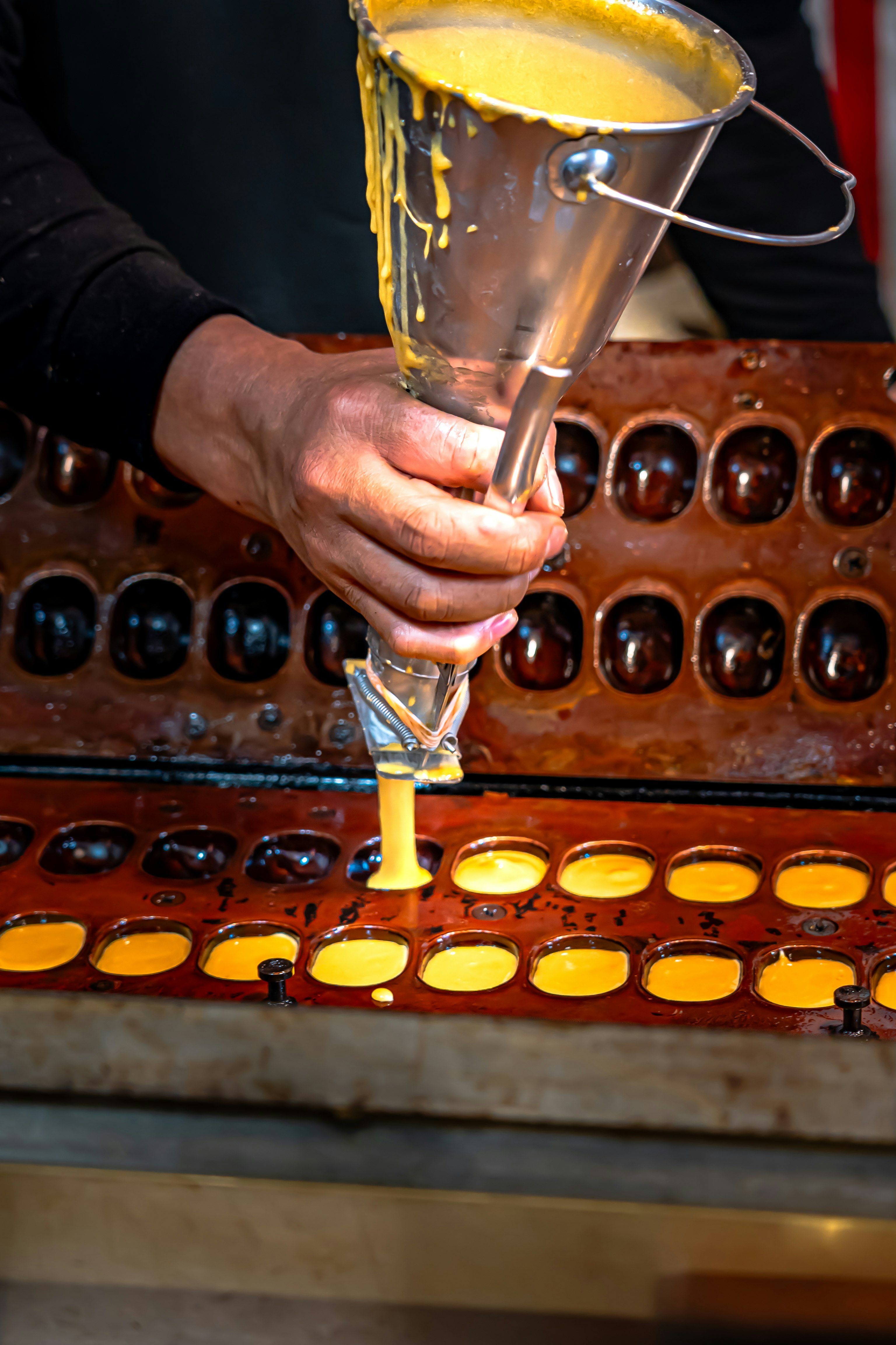 mano che versa un liquido dorato in una fila di piccoli contenitori color rame