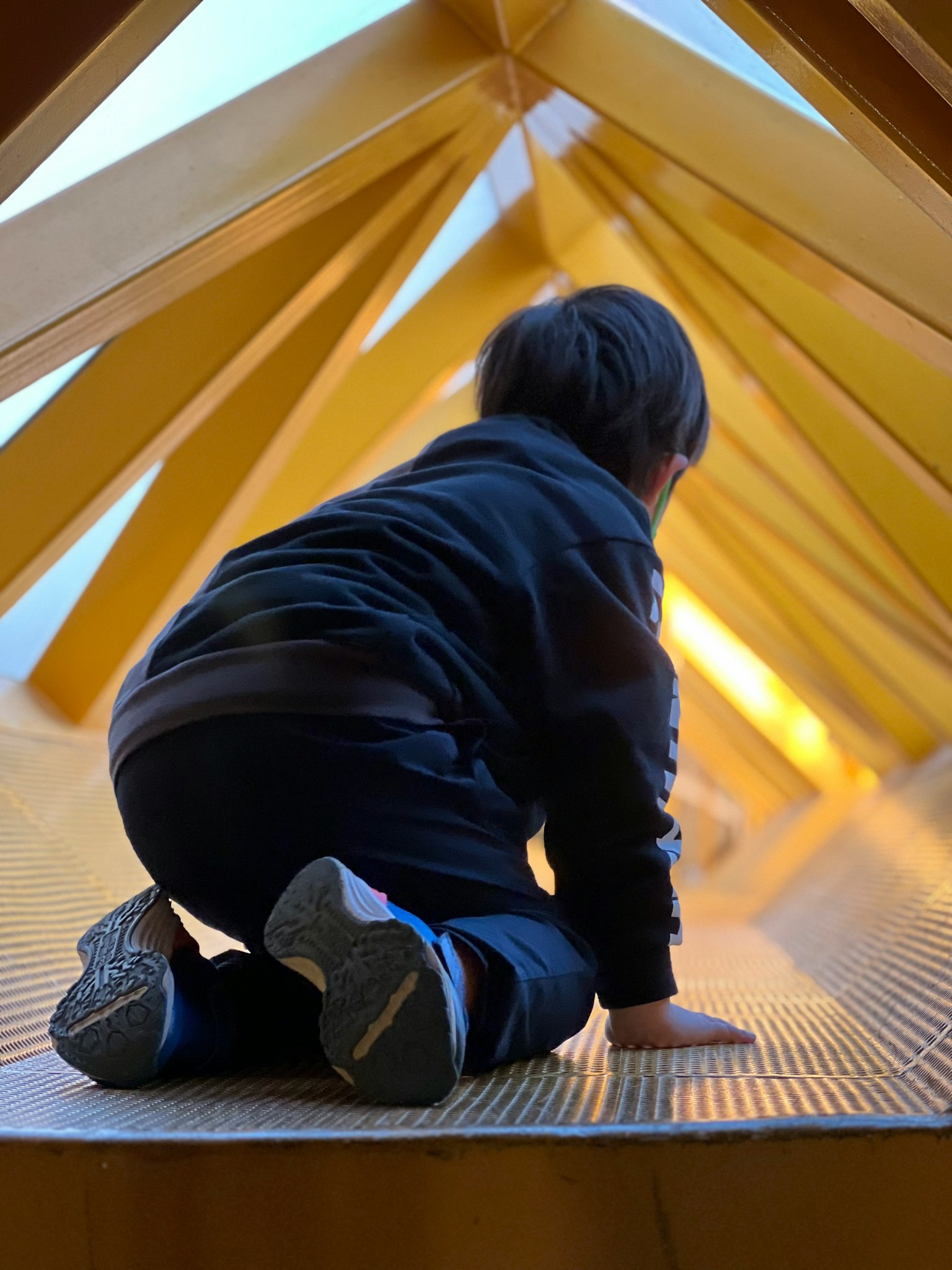 Un niño gateando dentro de una estructura con vigas de madera amarillas visibles