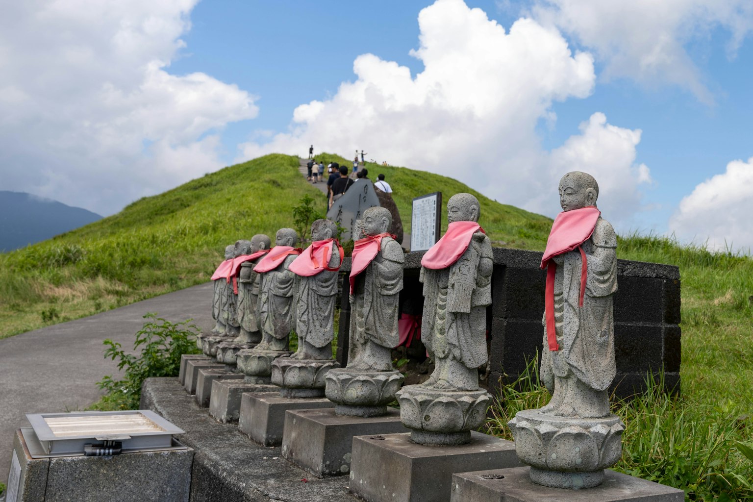 Stone statues lined up on a hillside wearing pink scarves