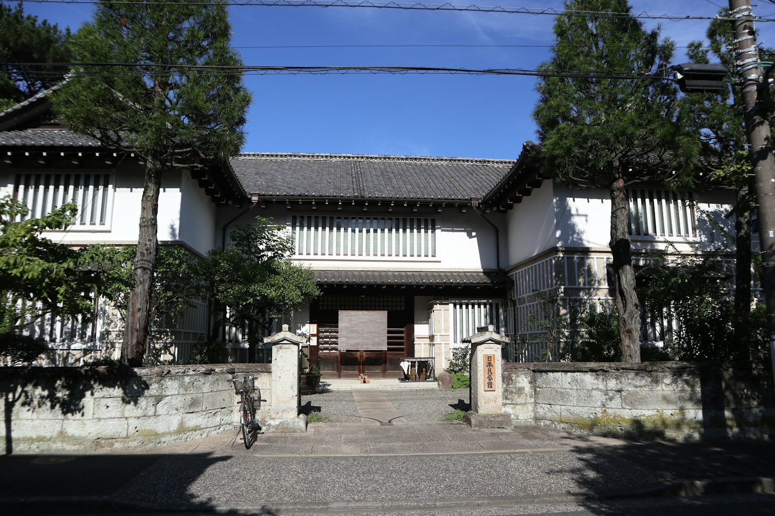 傳統日本房屋外觀，白色牆壁和木柱，周圍被綠色植物包圍