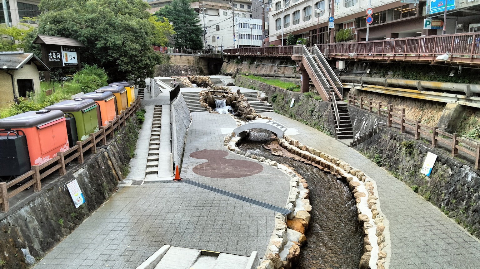 Pemandangan sungai di kota pemandian air panas dengan tanggul batu dan kendaraan berwarna-warni