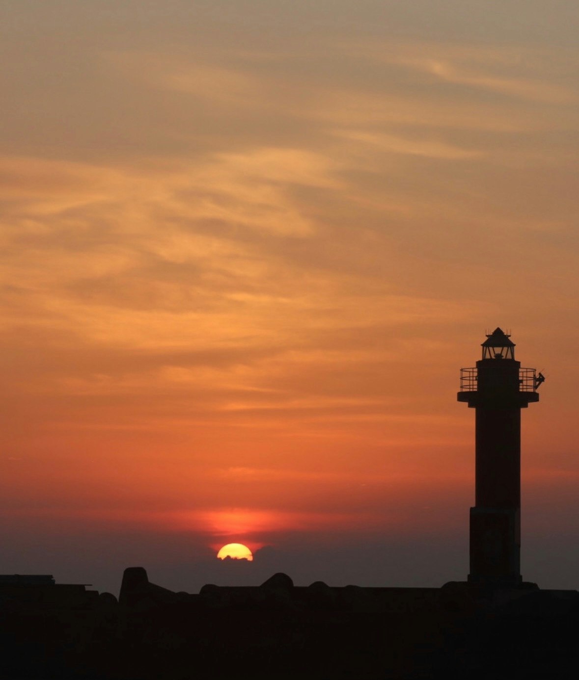 夕焼け空と海辺の灯台のシルエット