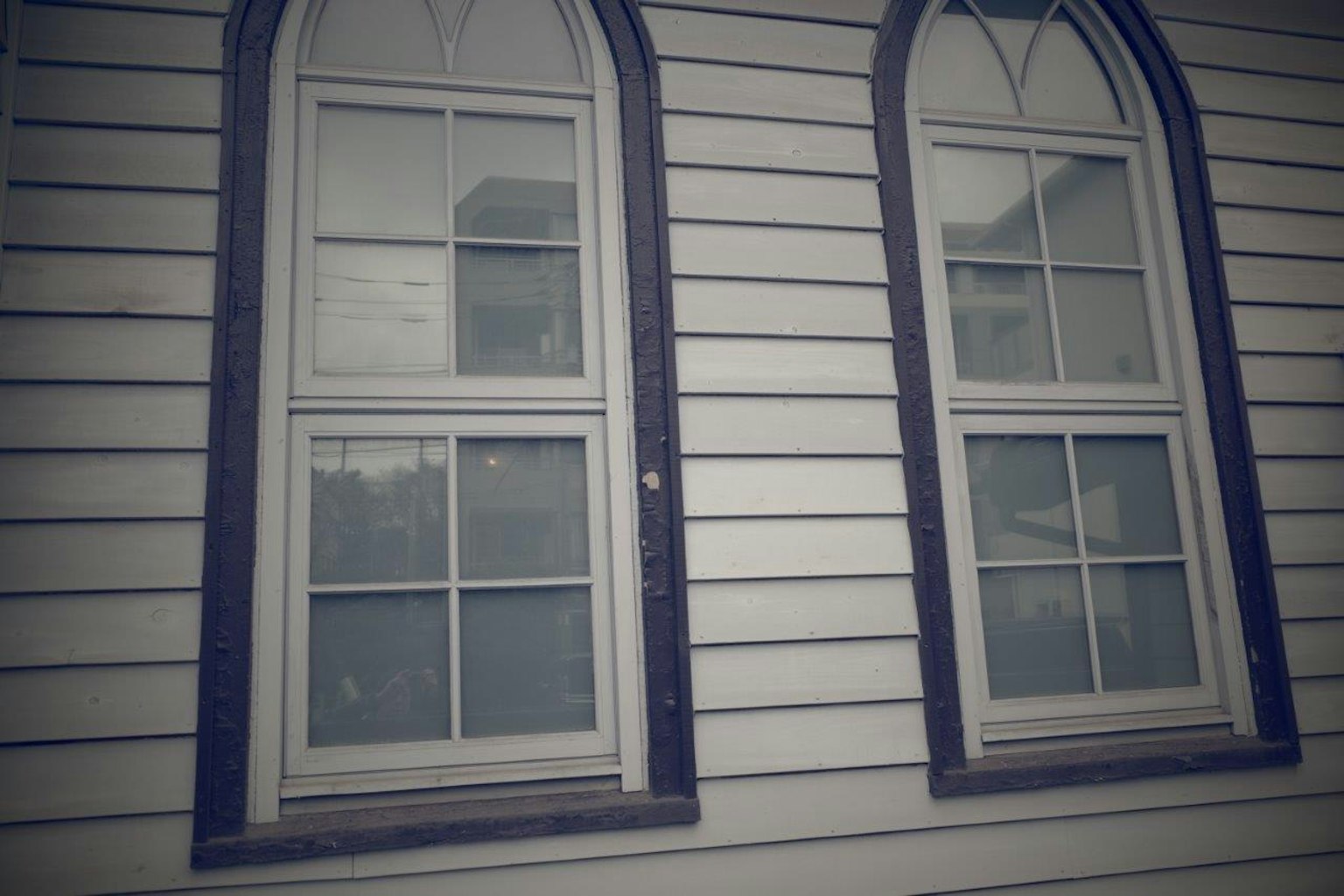 Two arched windows on a white wooden building exterior