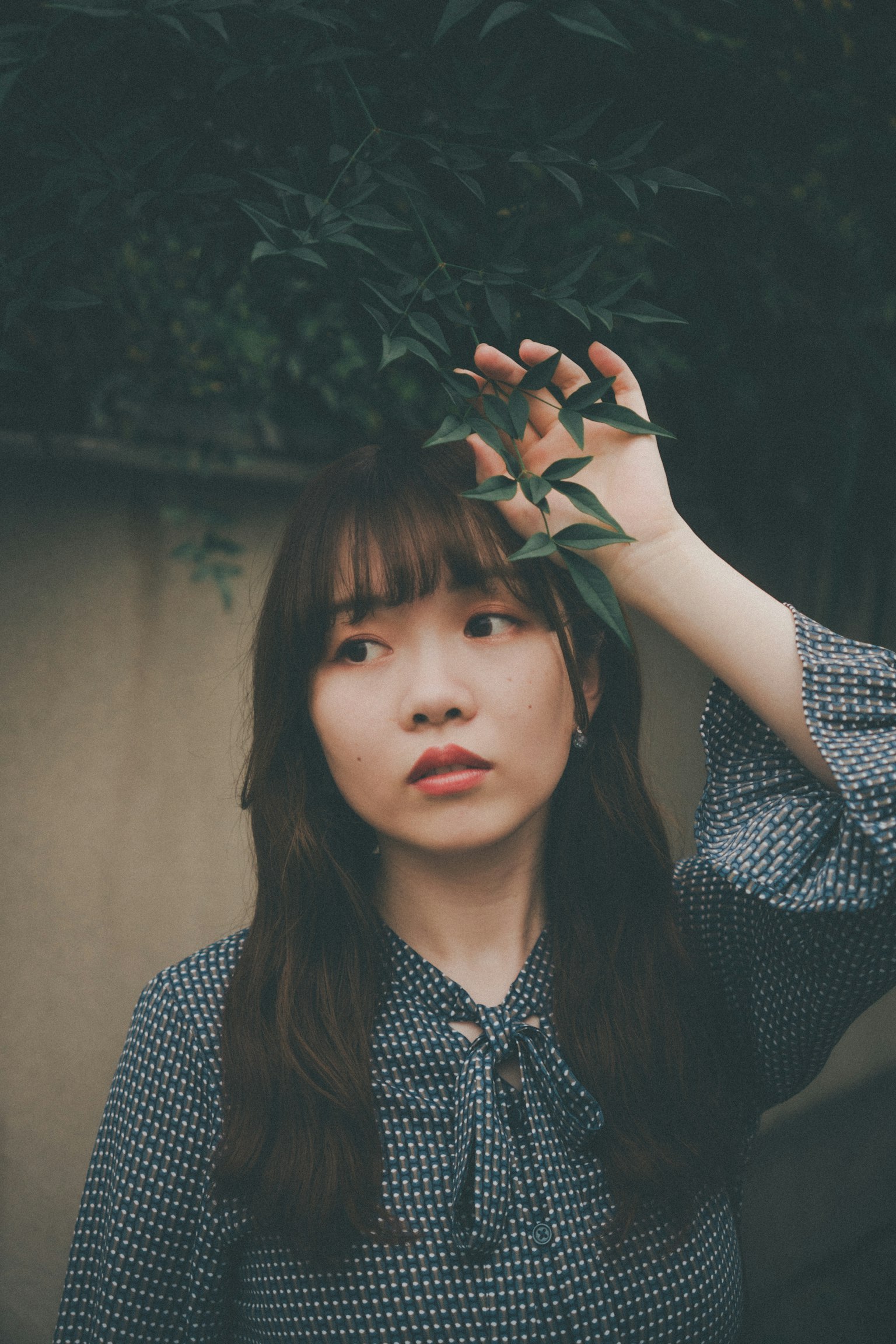 一位女性手持树叶，表情细腻，自然背景