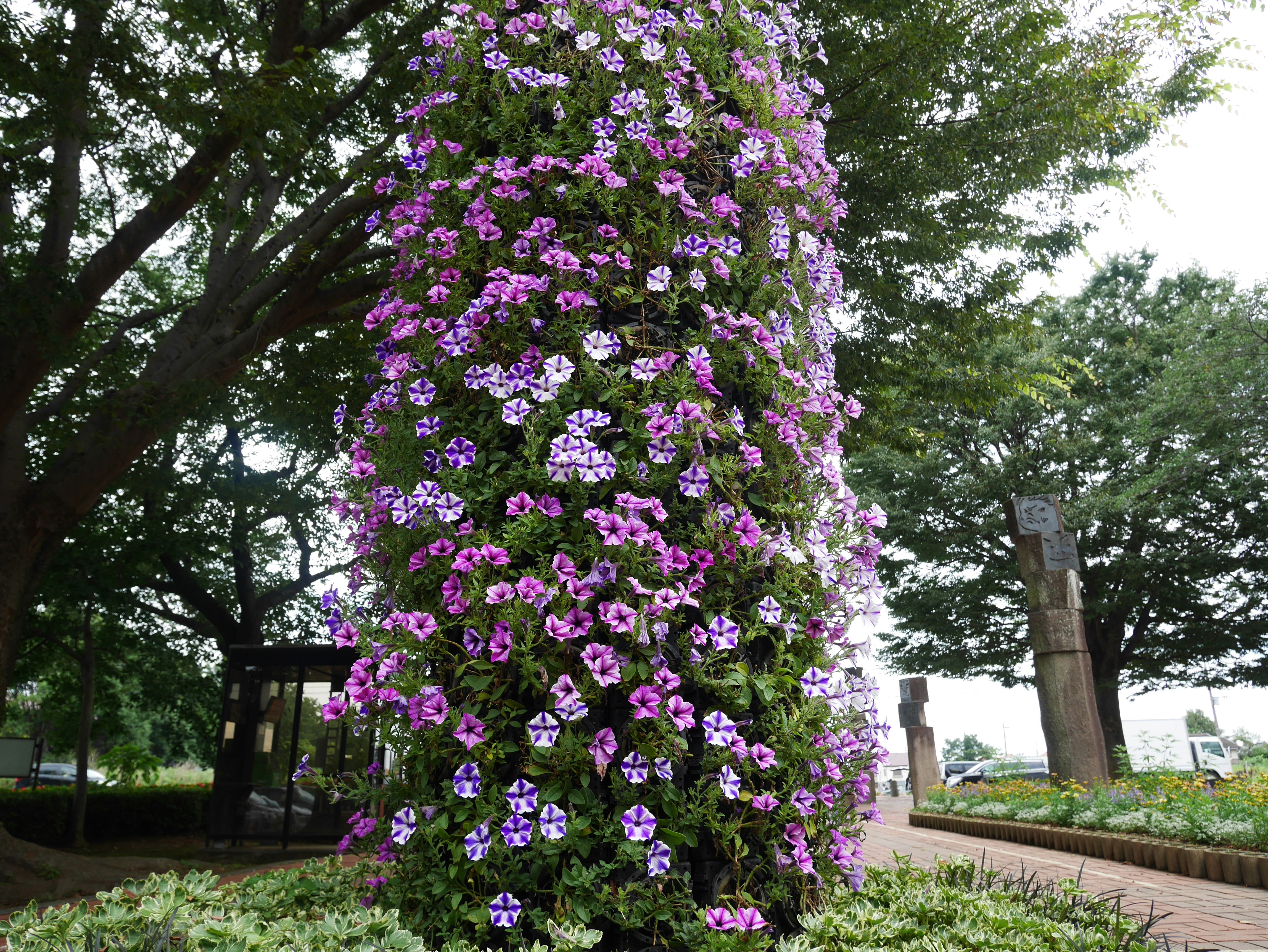 紫の花が咲く木の下の花壇と並木