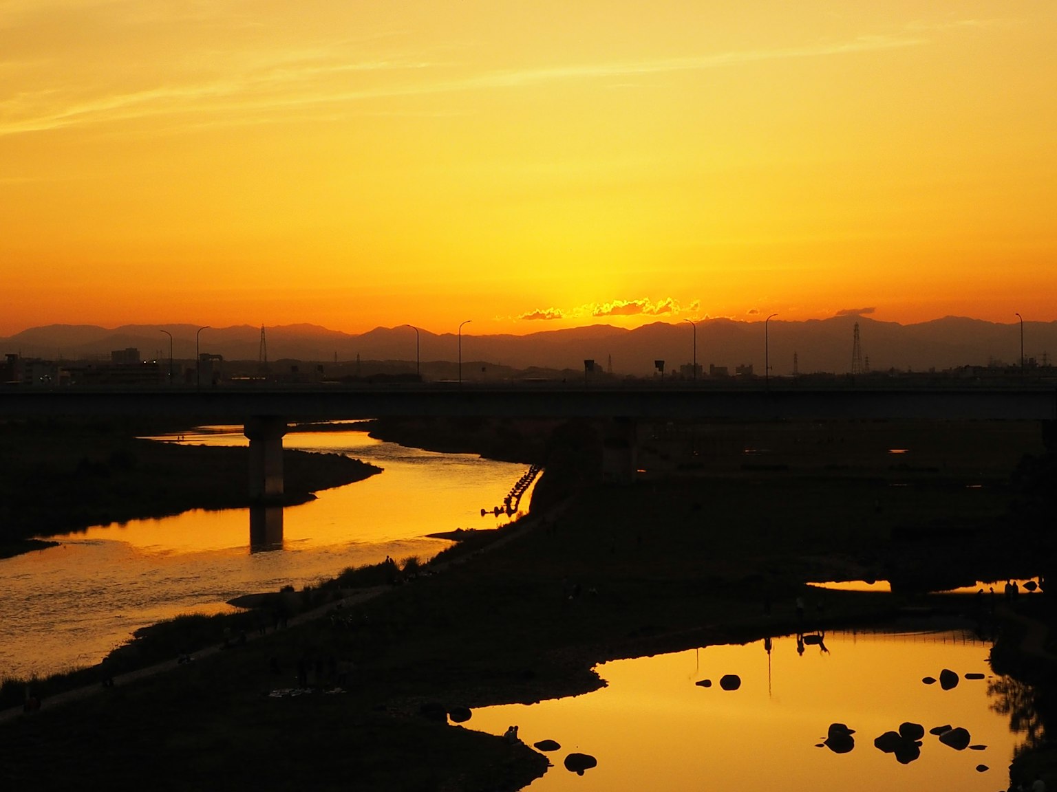 Vista escénica de un río reflejando el atardecer con siluetas de montañas