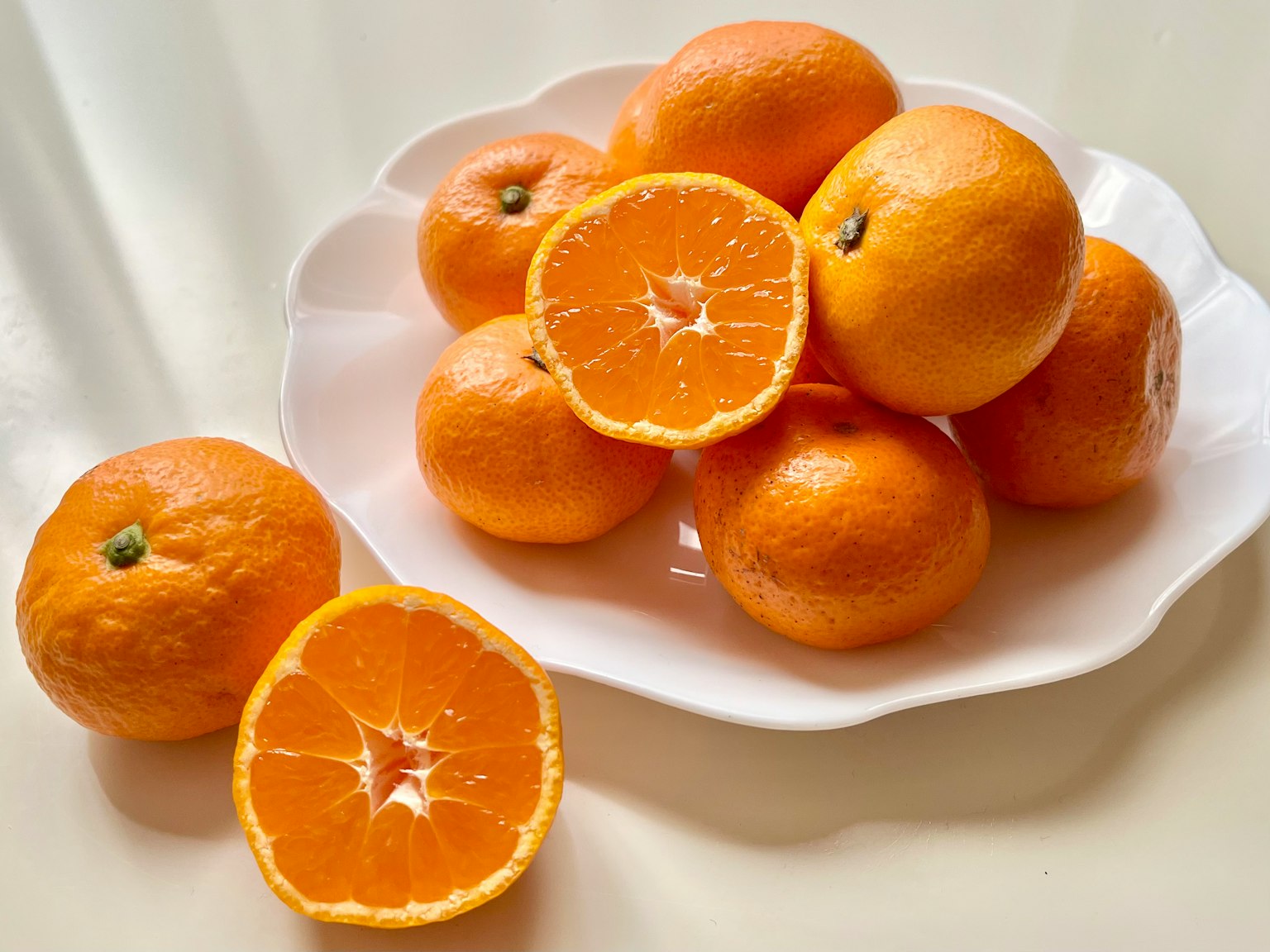 Un plato blanco con naranjas enteras y cortadas mostrando colores naranjas vibrantes
