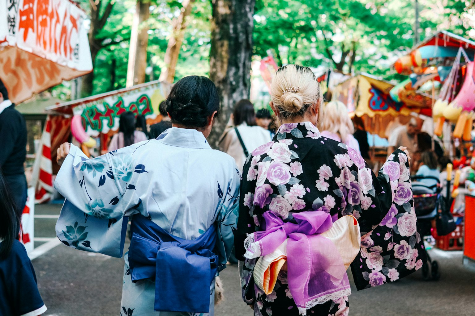 Zwei Frauen im Kimono gehen auf ein Festival zu bunte Stände im Hintergrund