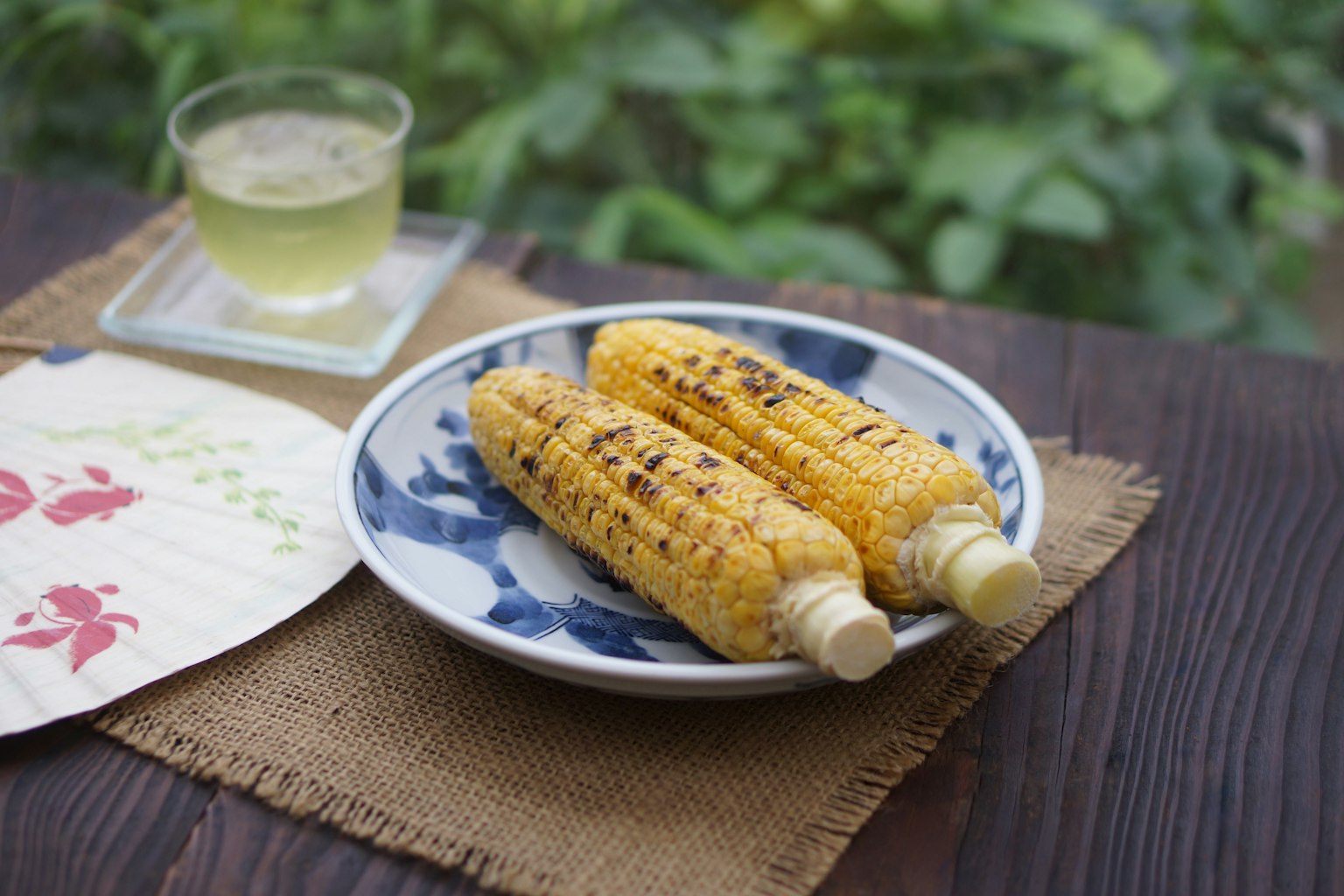 烤玉米放在盘子里，旁边有饮料，环境宁静