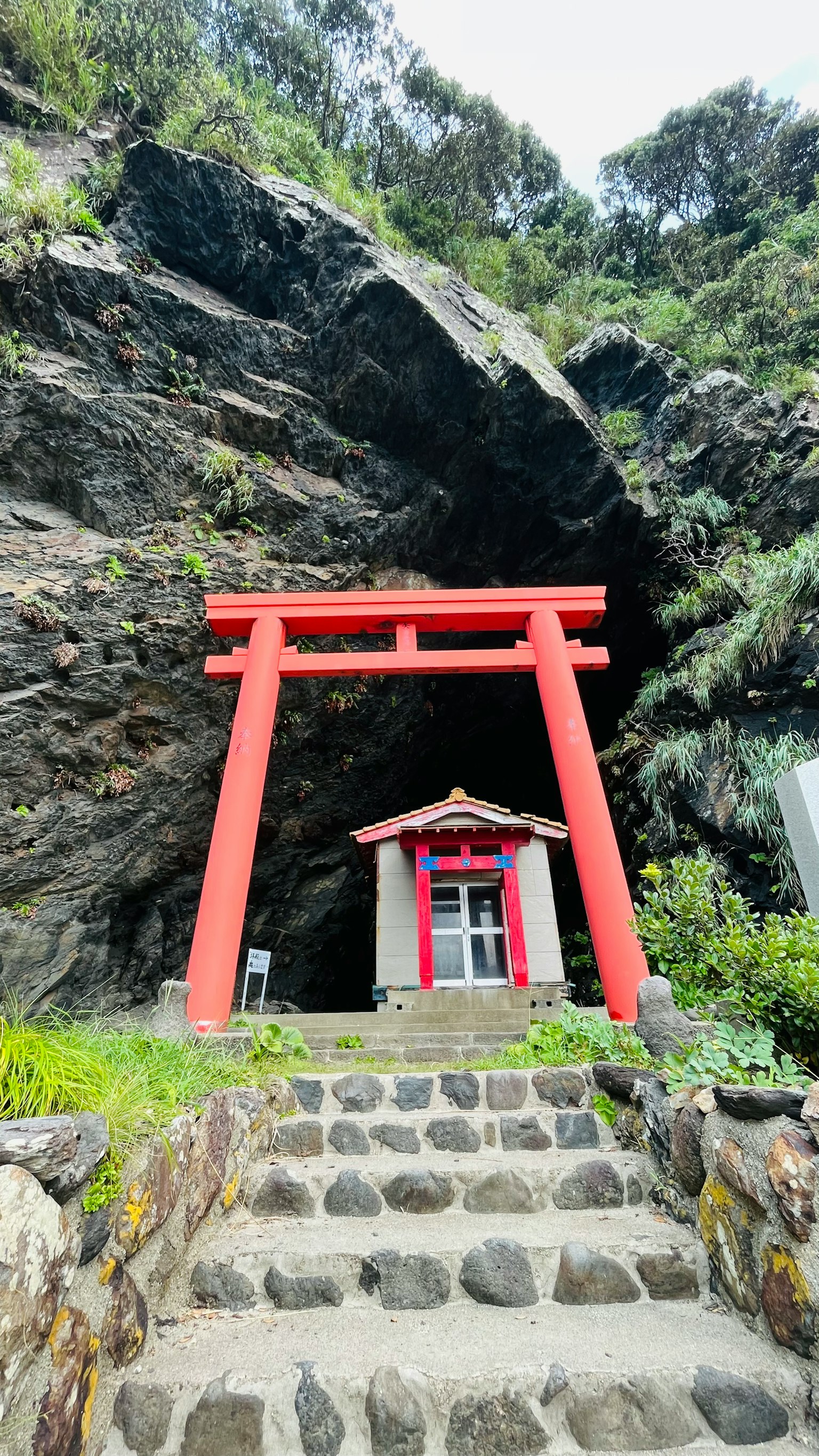 Red torii gate and small shrine at the entrance of a rocky cave