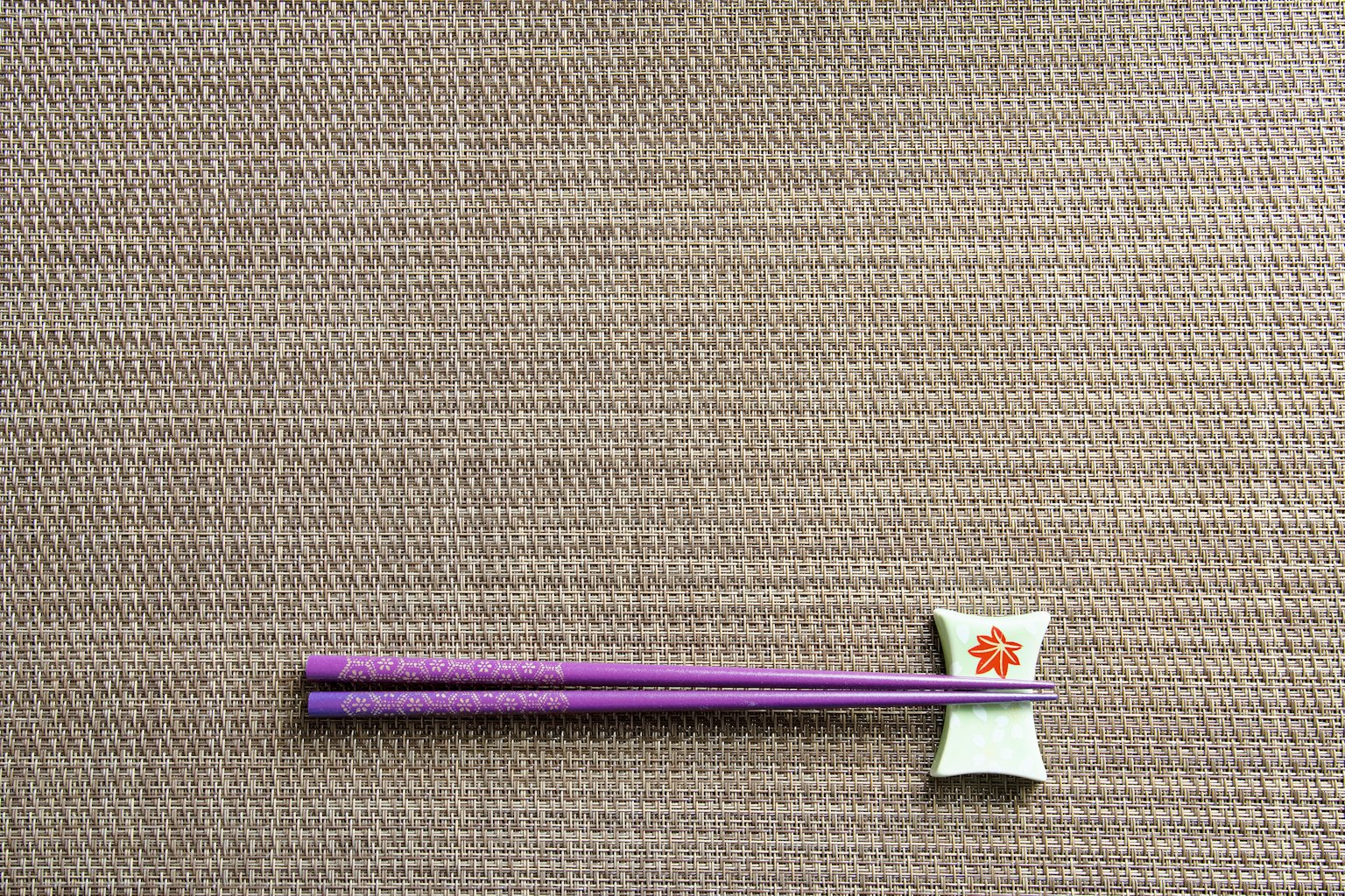 Des baguettes violettes et un repose-baguettes floral sur une table texturée