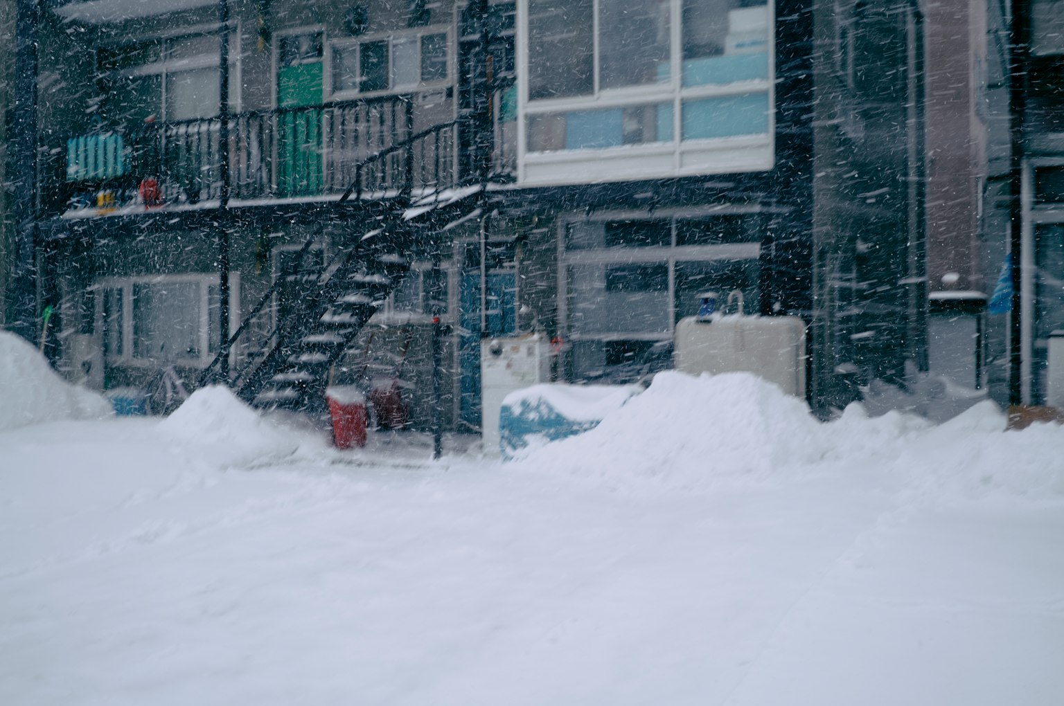 Vue extérieure d'un bâtiment recouvert de neige avec des escaliers visibles et une forte chute de neige