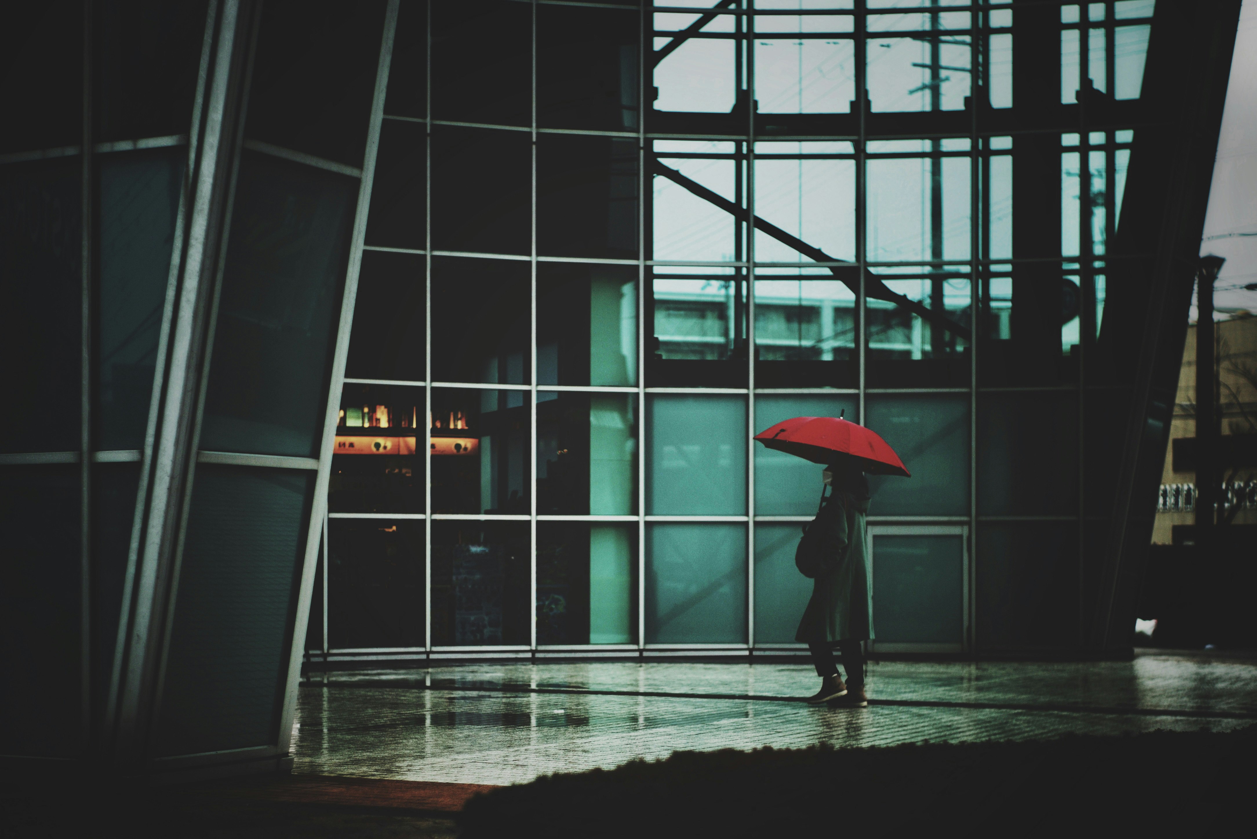雨の街角で傘をさす人と濡れた床のある路地