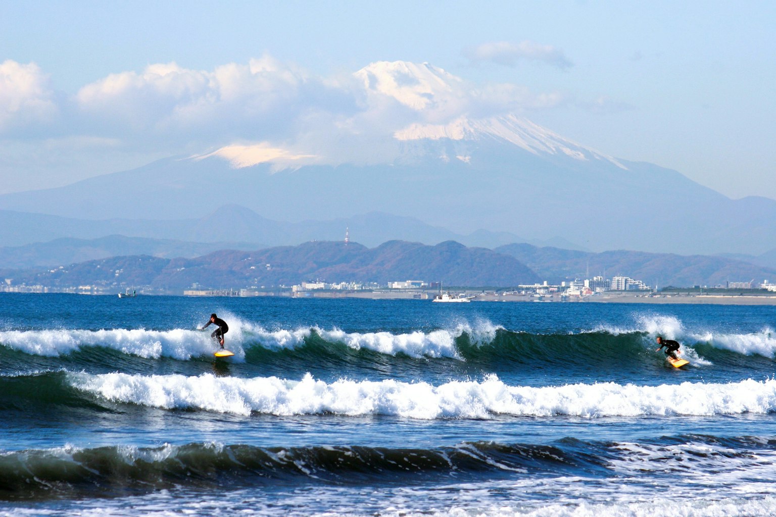 Due surfisti che cavalcano le onde nell'oceano con una montagna innevata sullo sfondo
