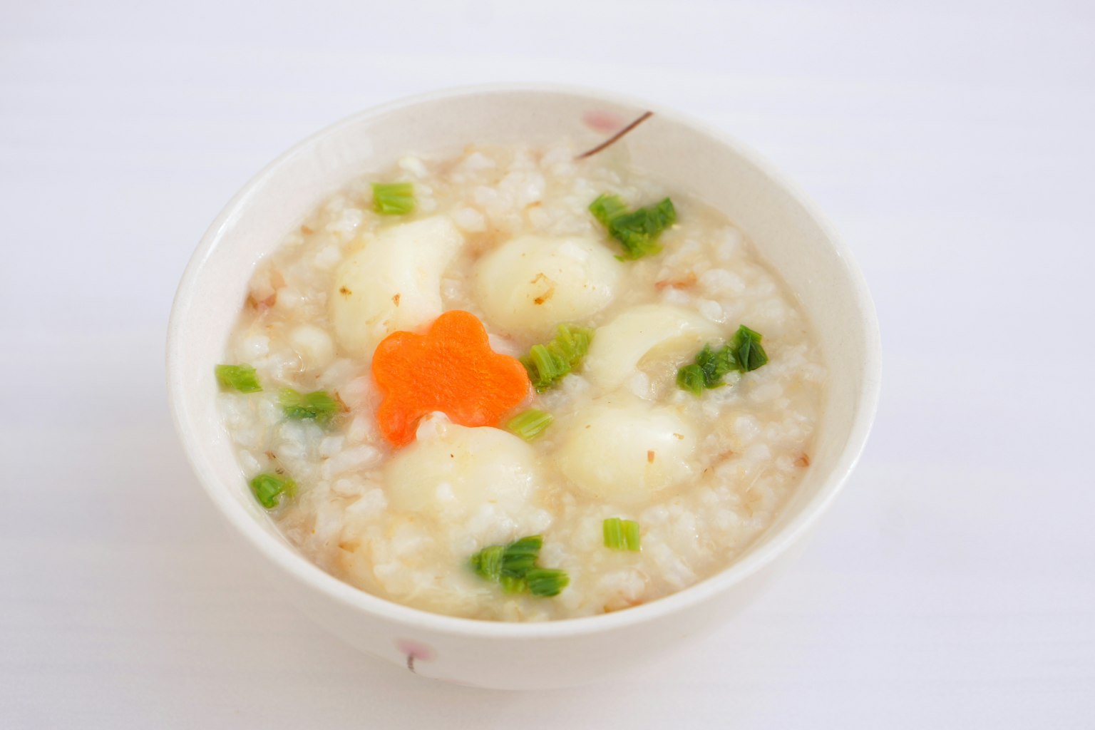 Una ciotola di porridge decorata con cipollotti e un fiore di carota arancione