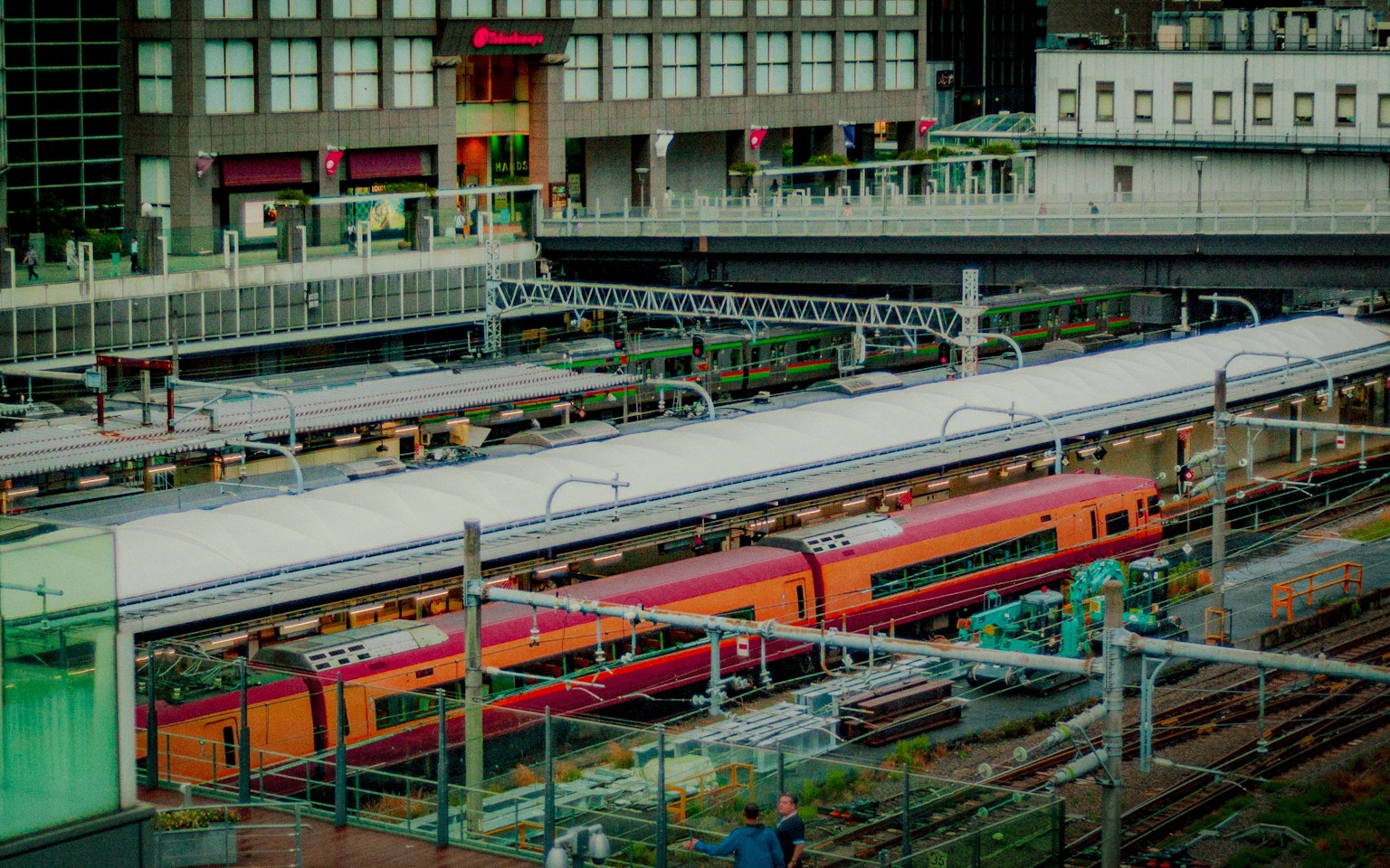 Trains colorés à une gare avec des voies ferrées et des bâtiments modernes visibles