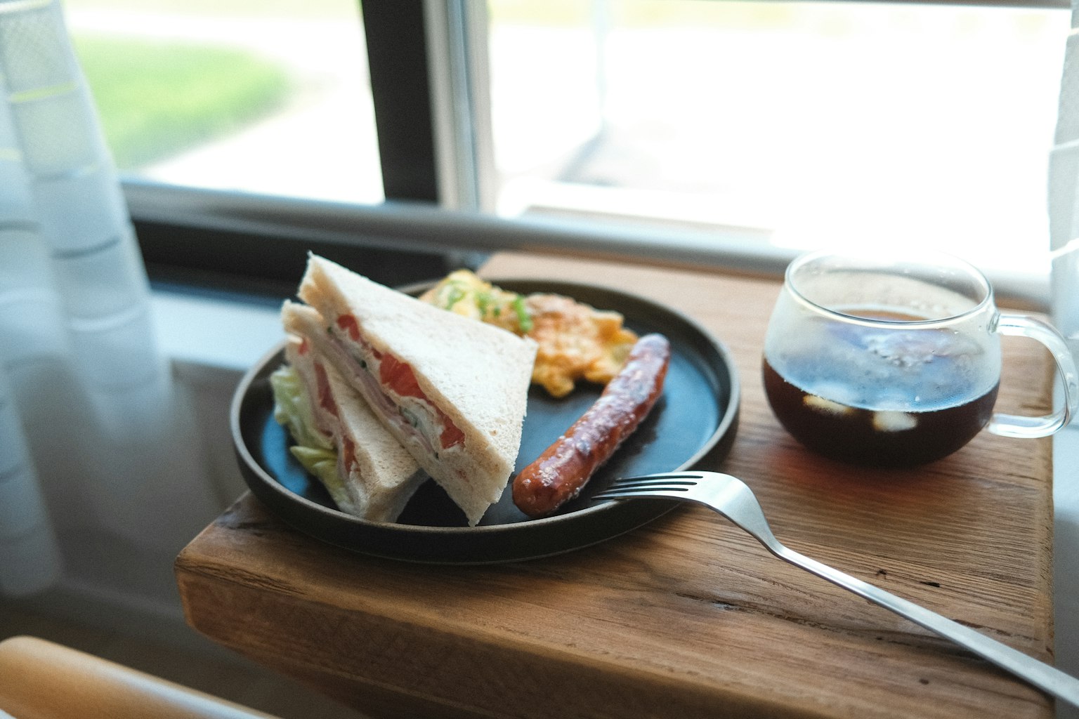 Un plato con sándwiches y salchicha sobre una mesa de madera junto a un vaso de té