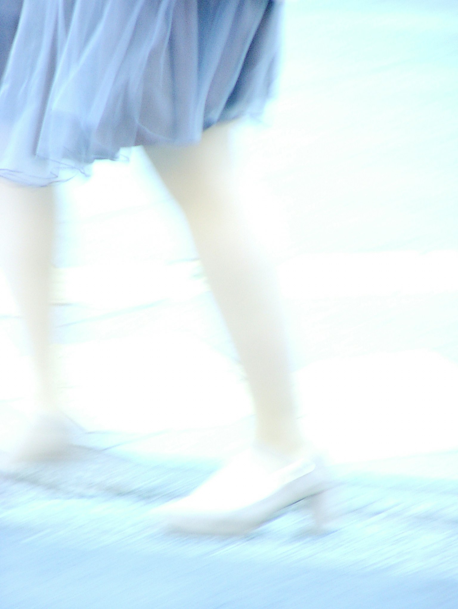 A blurred image of a woman walking in a light blue skirt and shoes