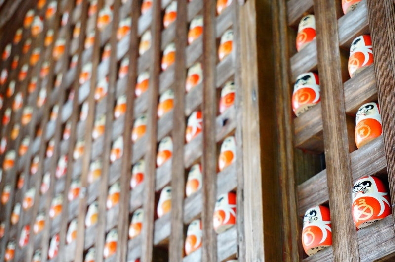 だるまが並ぶ木格子の祈願小物のある寺の風景