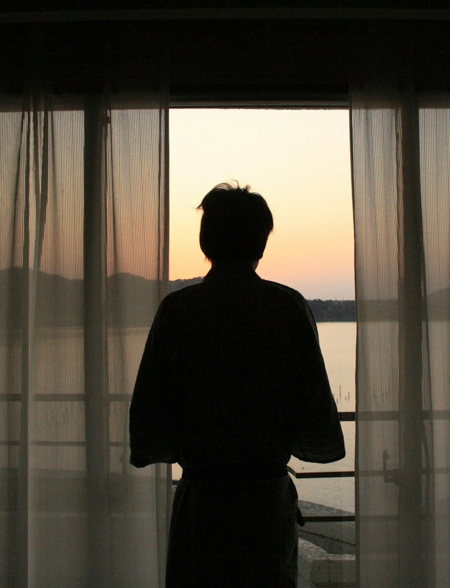Silhouette d'une personne se tenant devant une fenêtre avec un coucher de soleil en arrière-plan