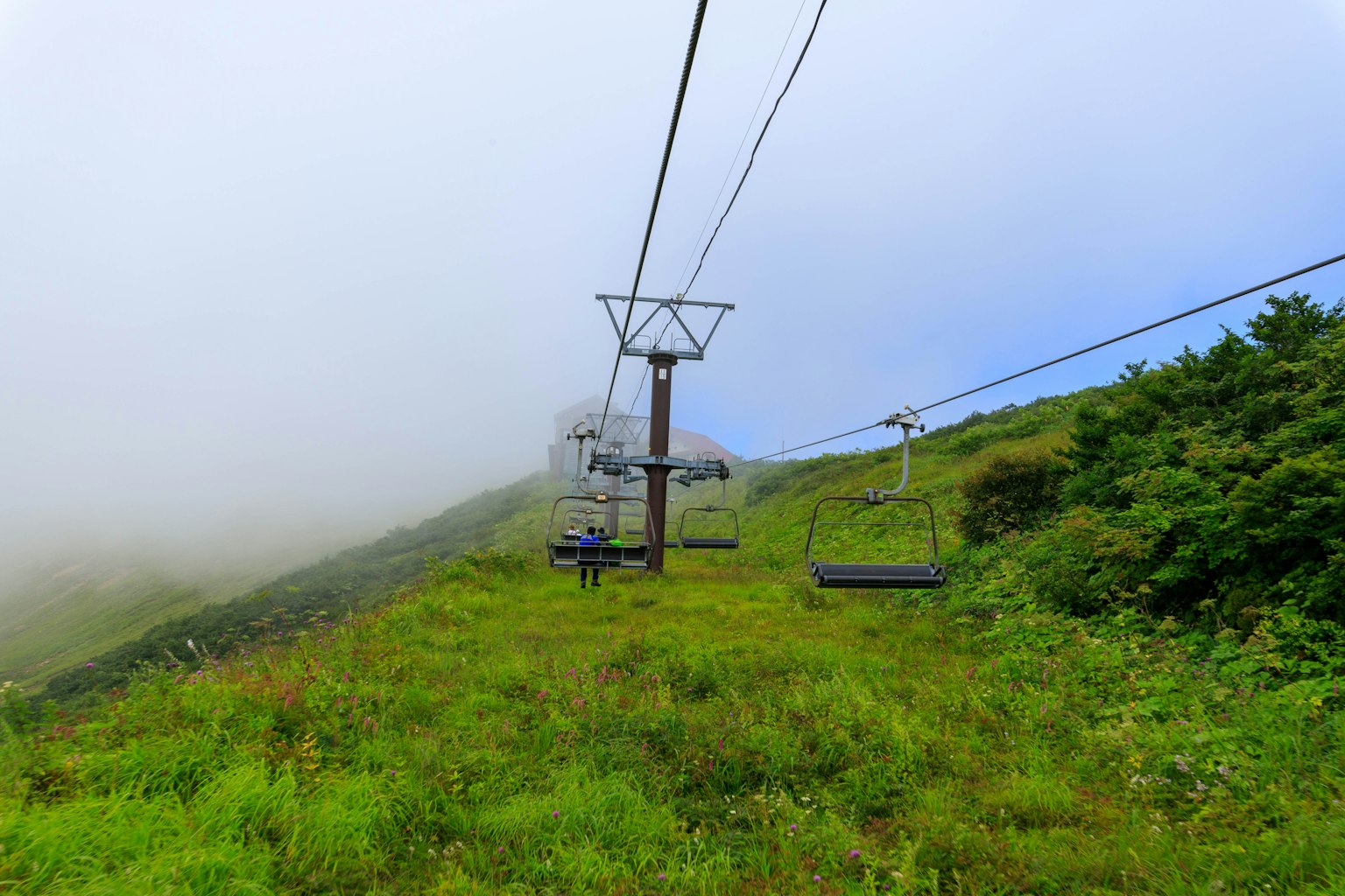 Télésiège sur une pente de montagne brumeuse entourée d'herbe verte